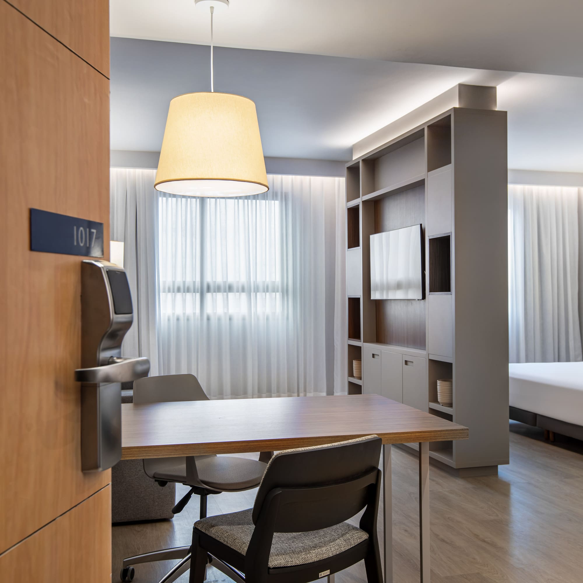 Modern hotel suite 1017 with bed, dining table, and TV unit.