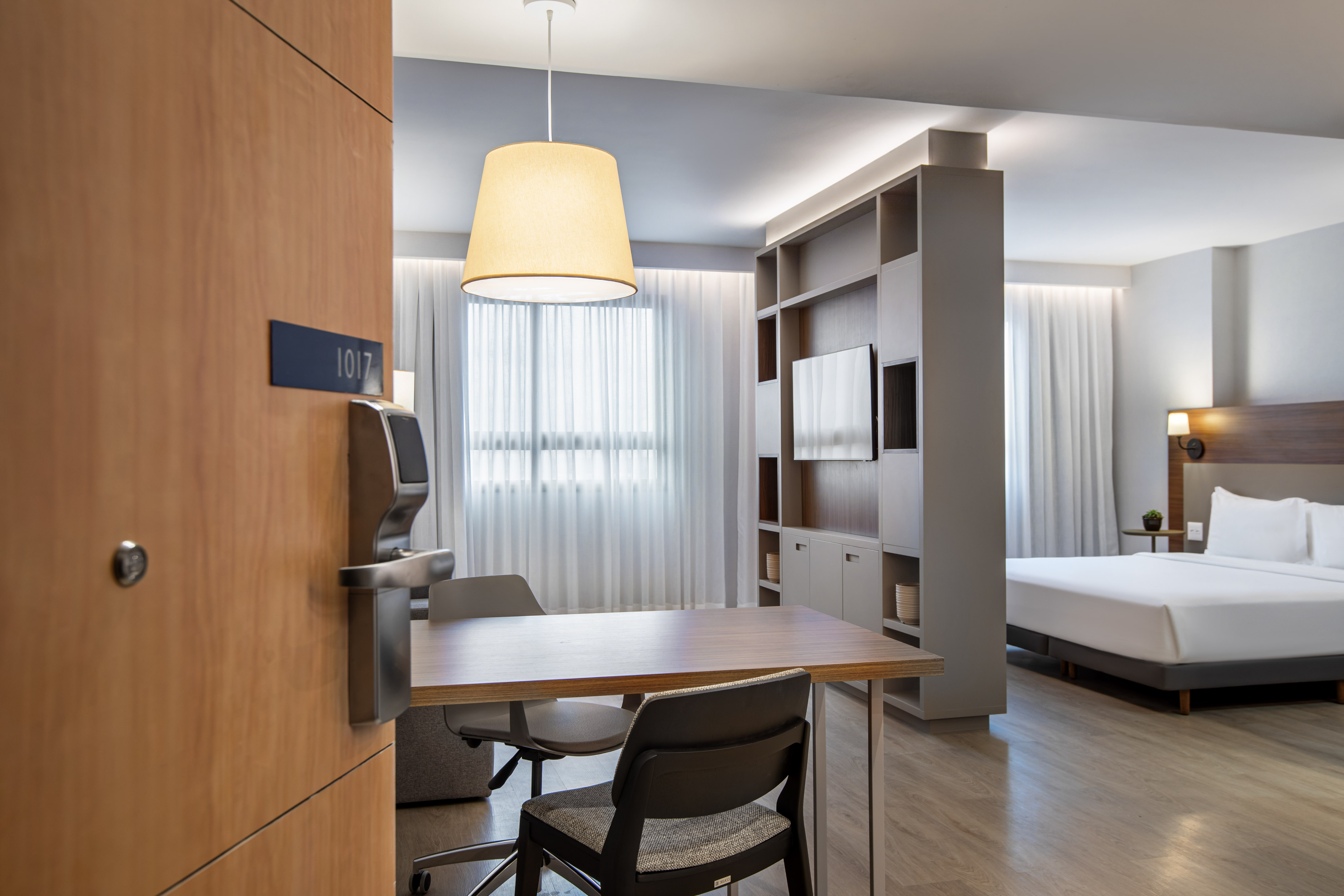Modern hotel suite 1017 with bed, dining table, and TV unit.