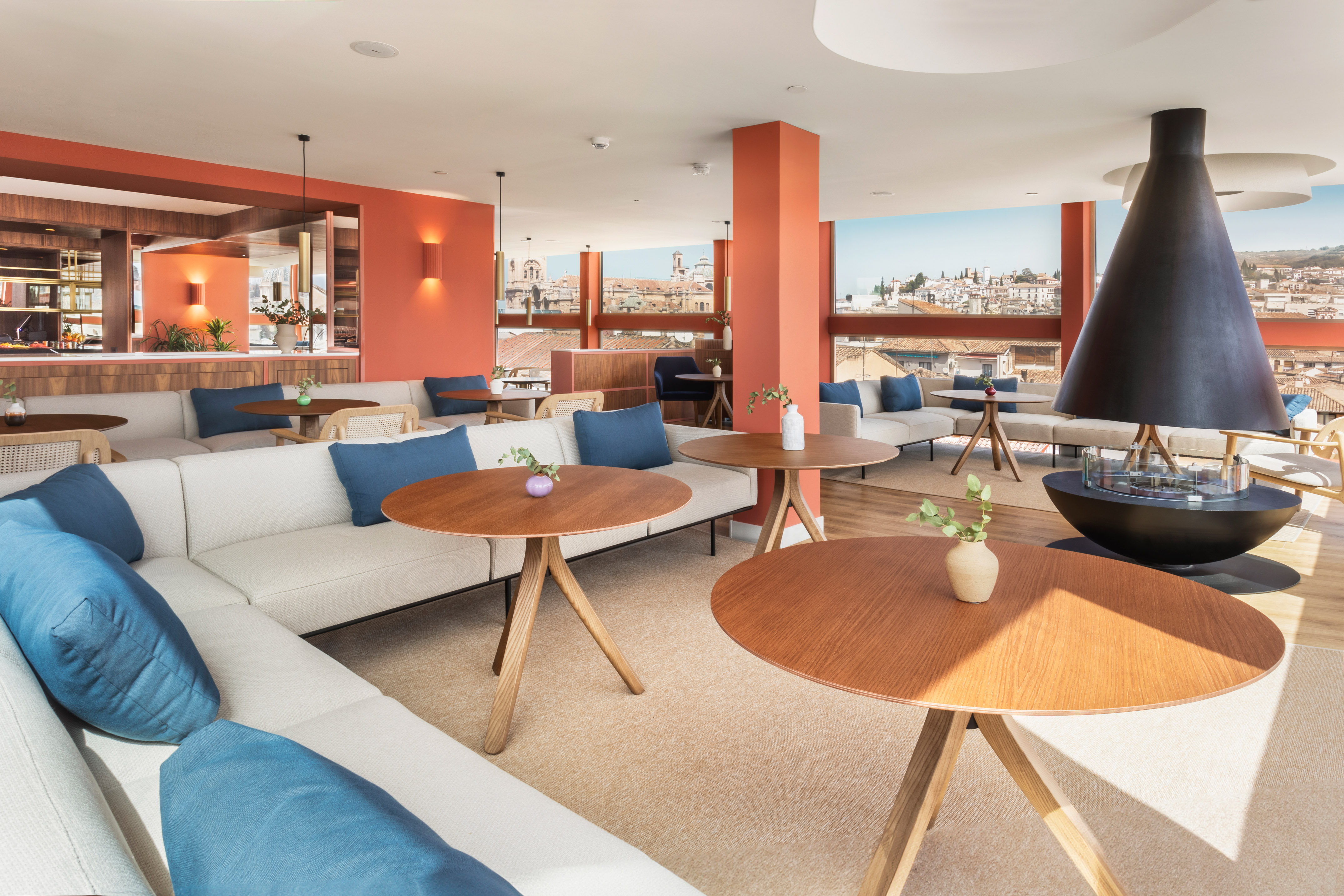 Modern lounge with city view, cream sofas, orange walls, and sleek fireplace.