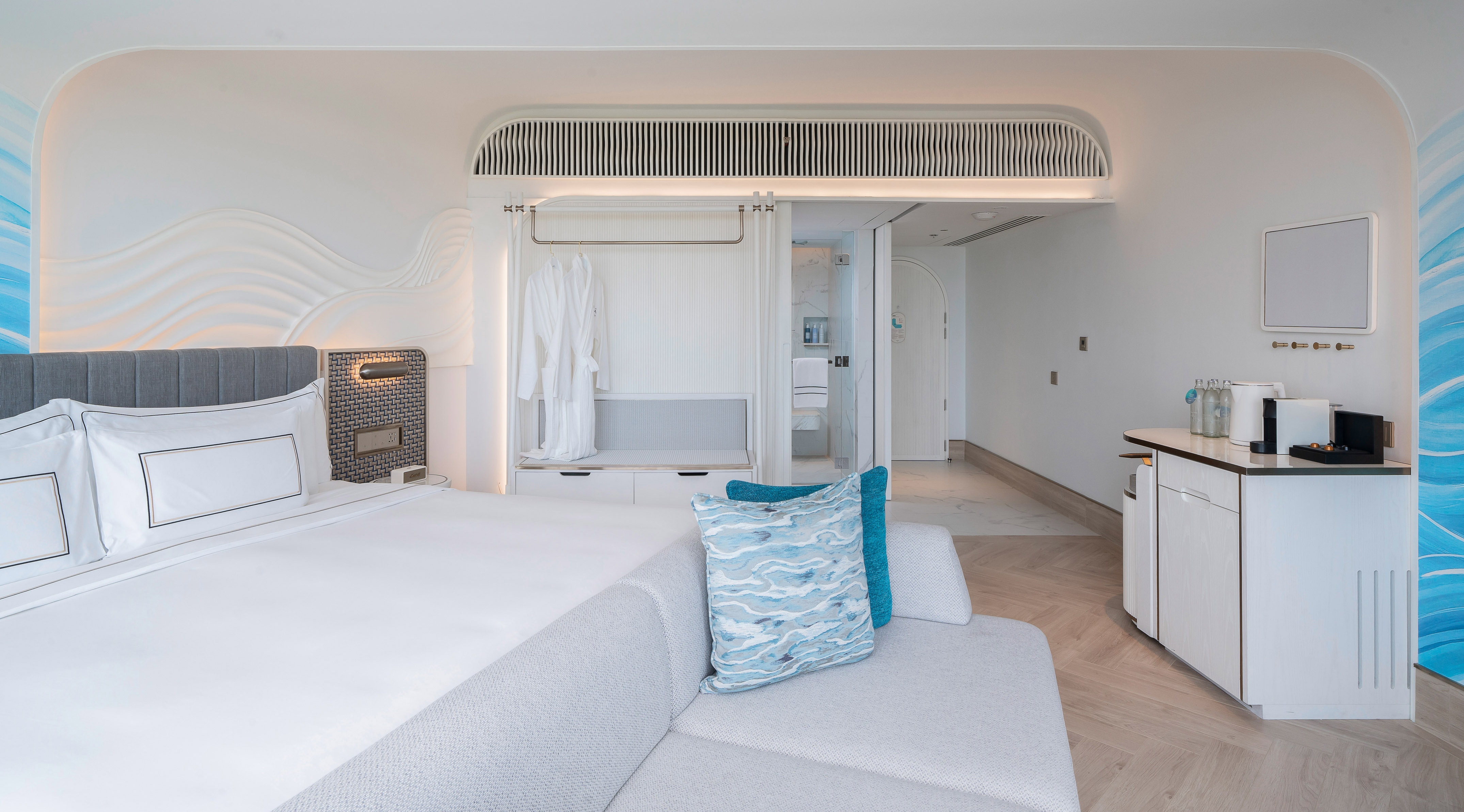 Modern hotel room with large bed, sofa, built-in storage, and wave decor.