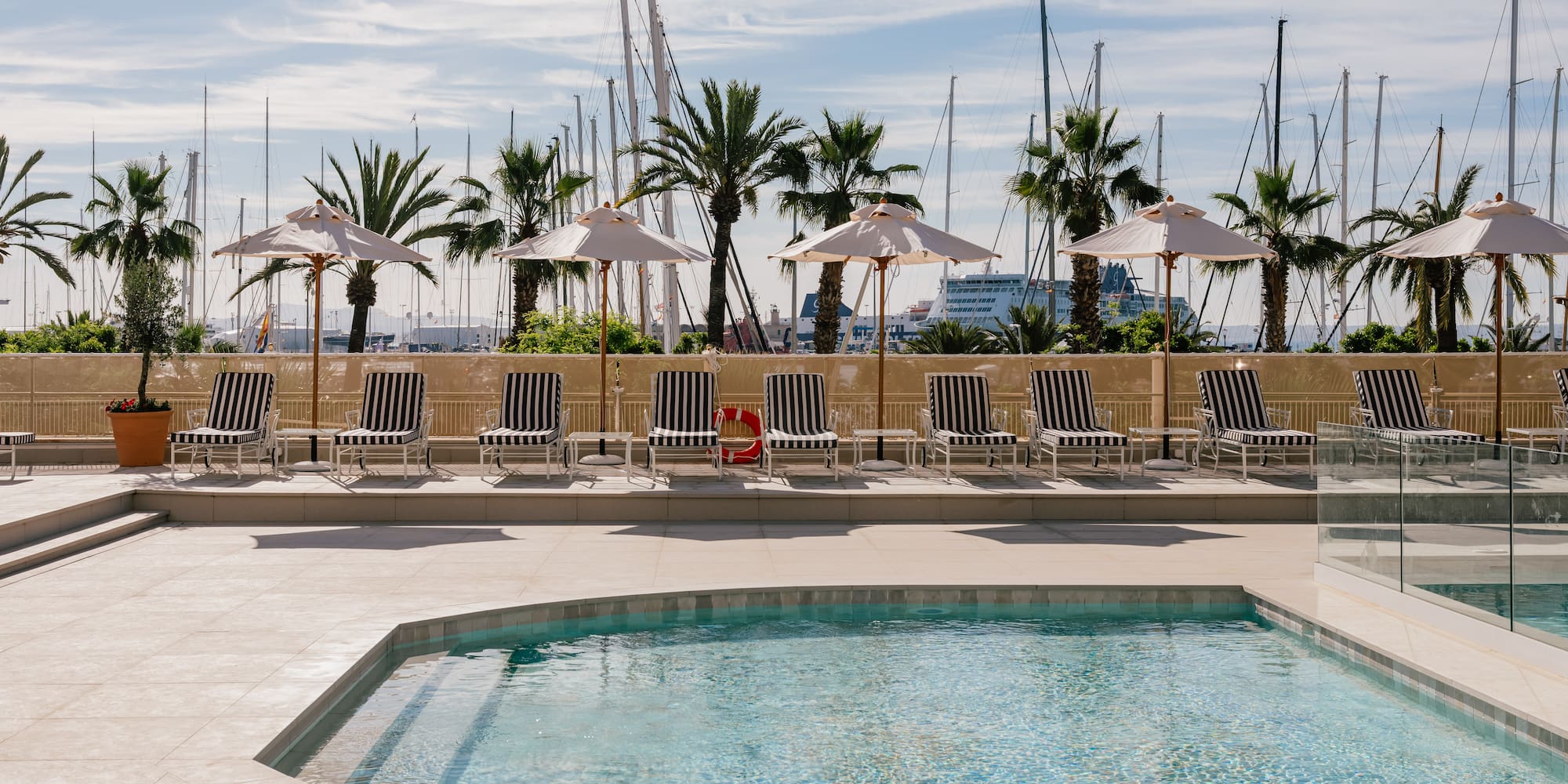 a pool with umbrellas and chairs by a building with boats in the background
