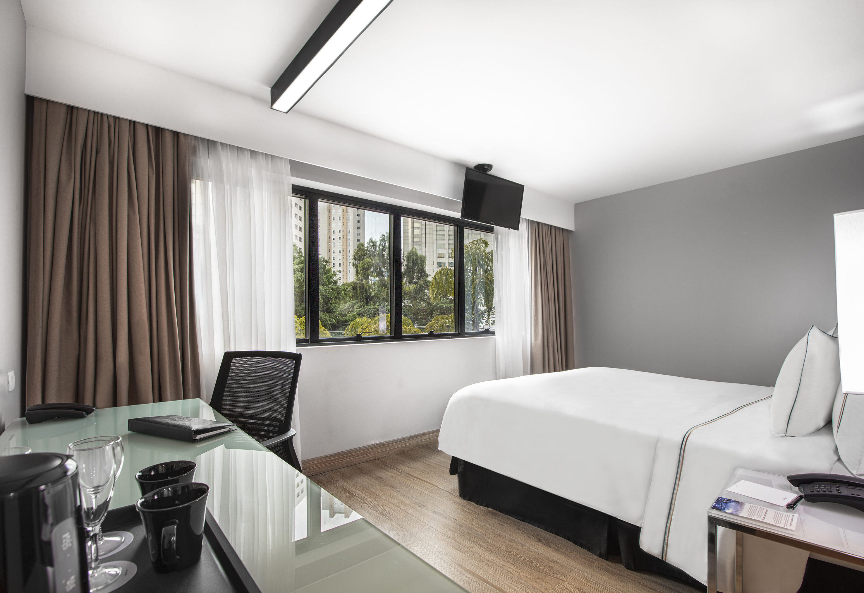 Modern hotel room with bed, work desk, TV, and city view window.