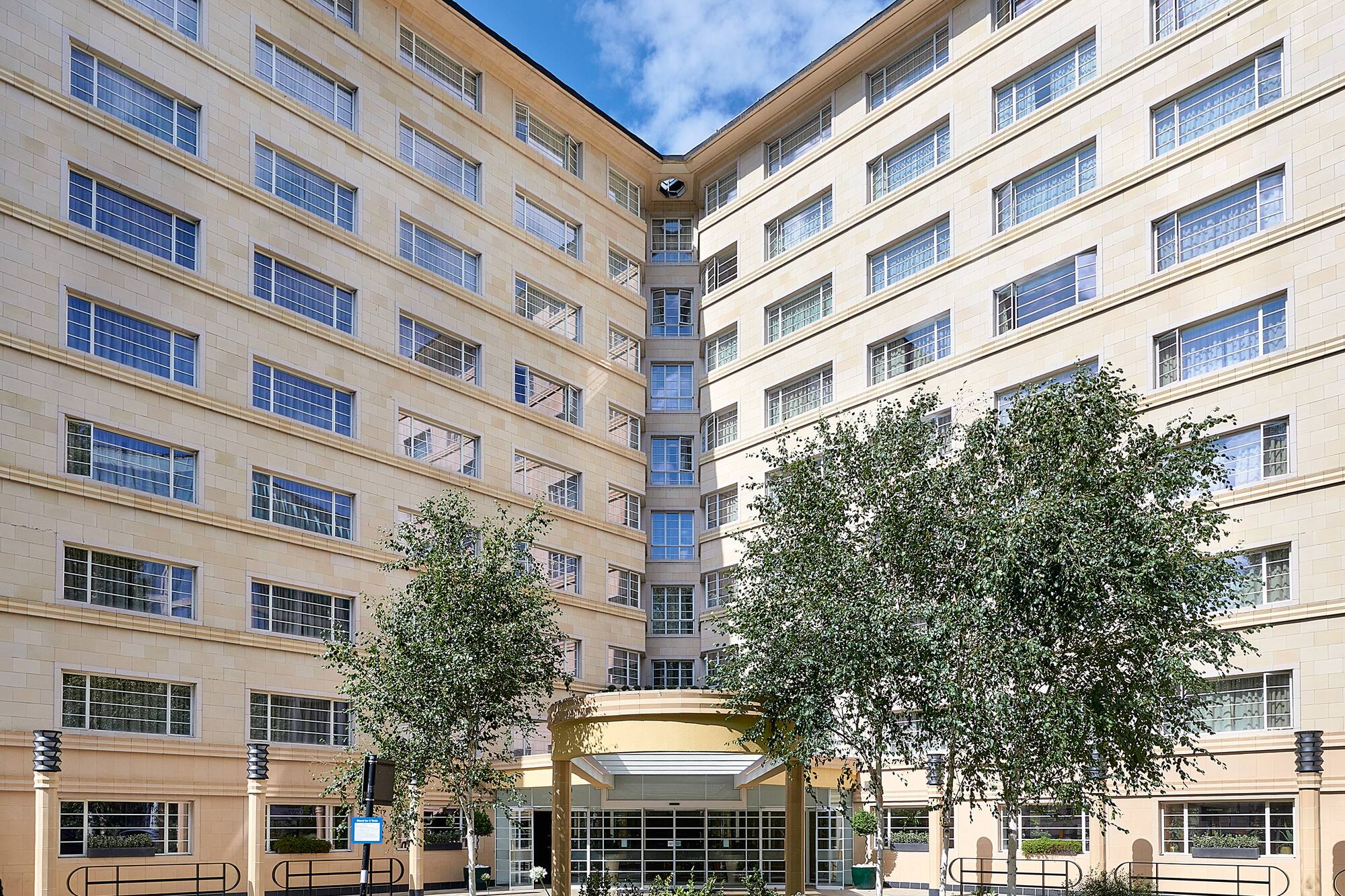 V-shaped modern building facade with trees and a street marked "TAXI".