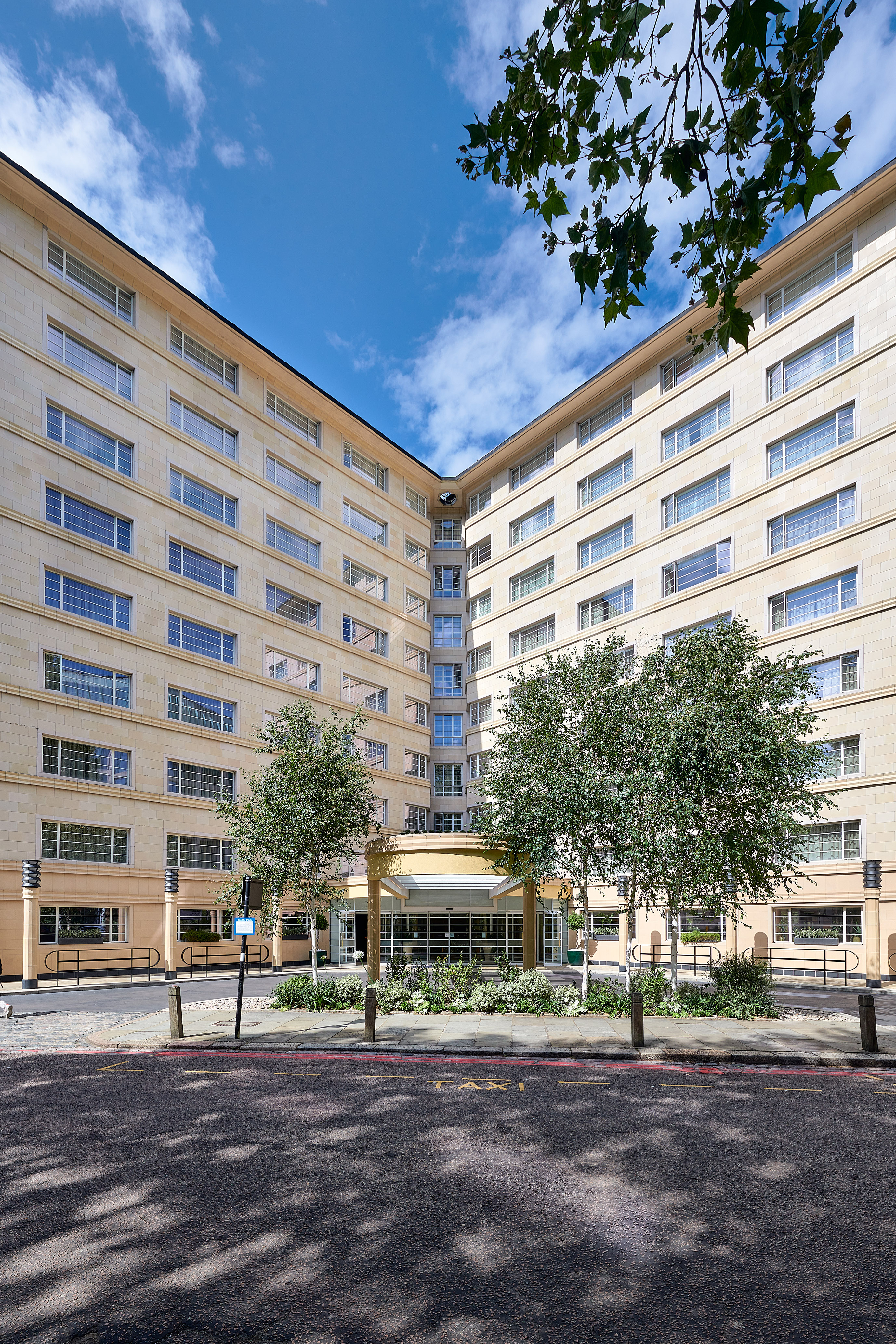 V-shaped modern building facade with trees and a street marked "TAXI".