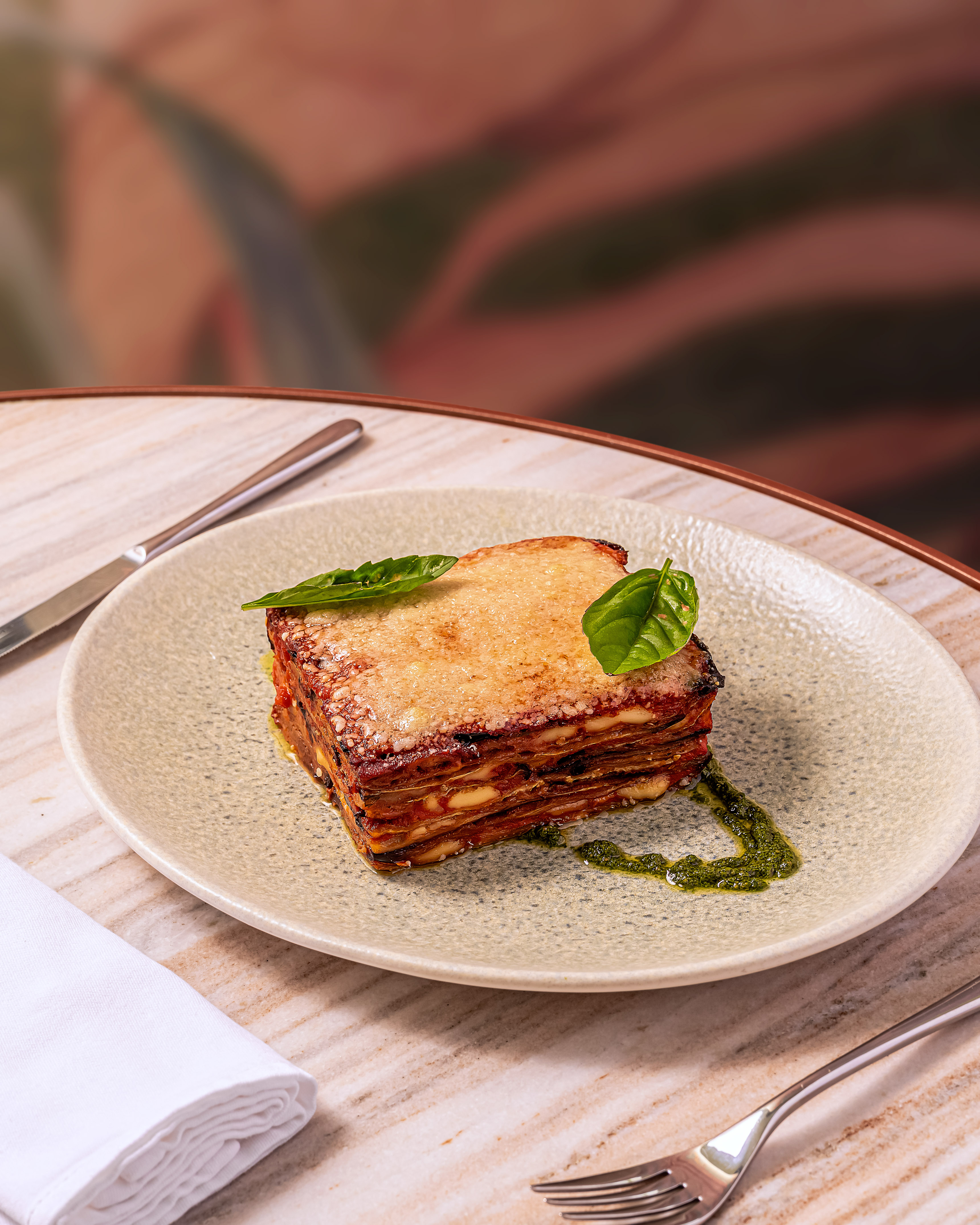 Classic lasagna slice with melted cheese, fresh basil, and pesto sauce.