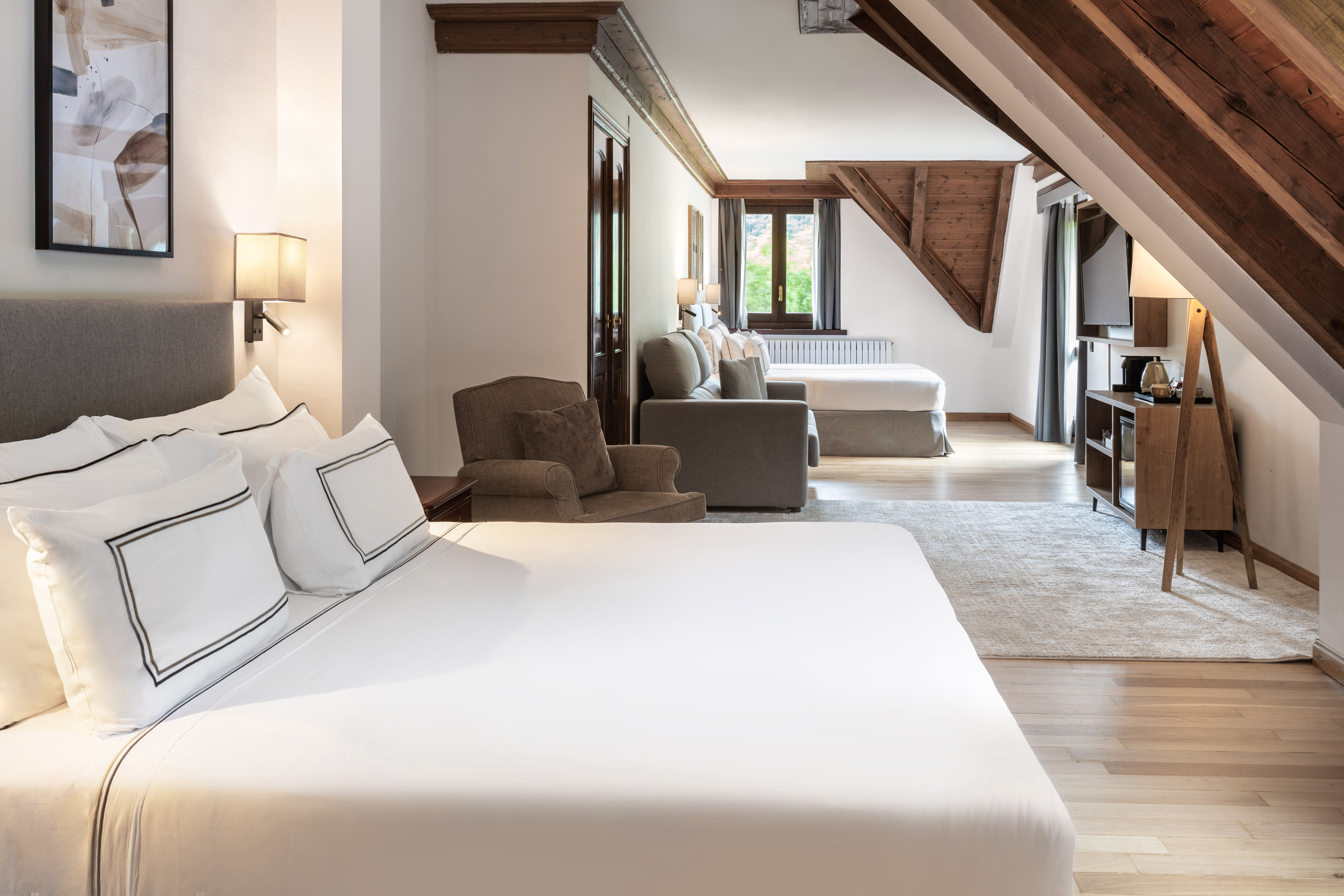 Amplia suite de hotel con dos camas, vigas de madera y zona de estar.