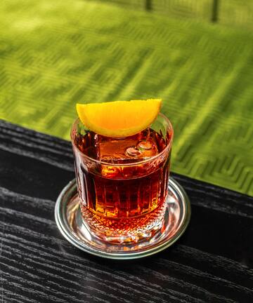 a glass of alcohol with a slice of orange on a table