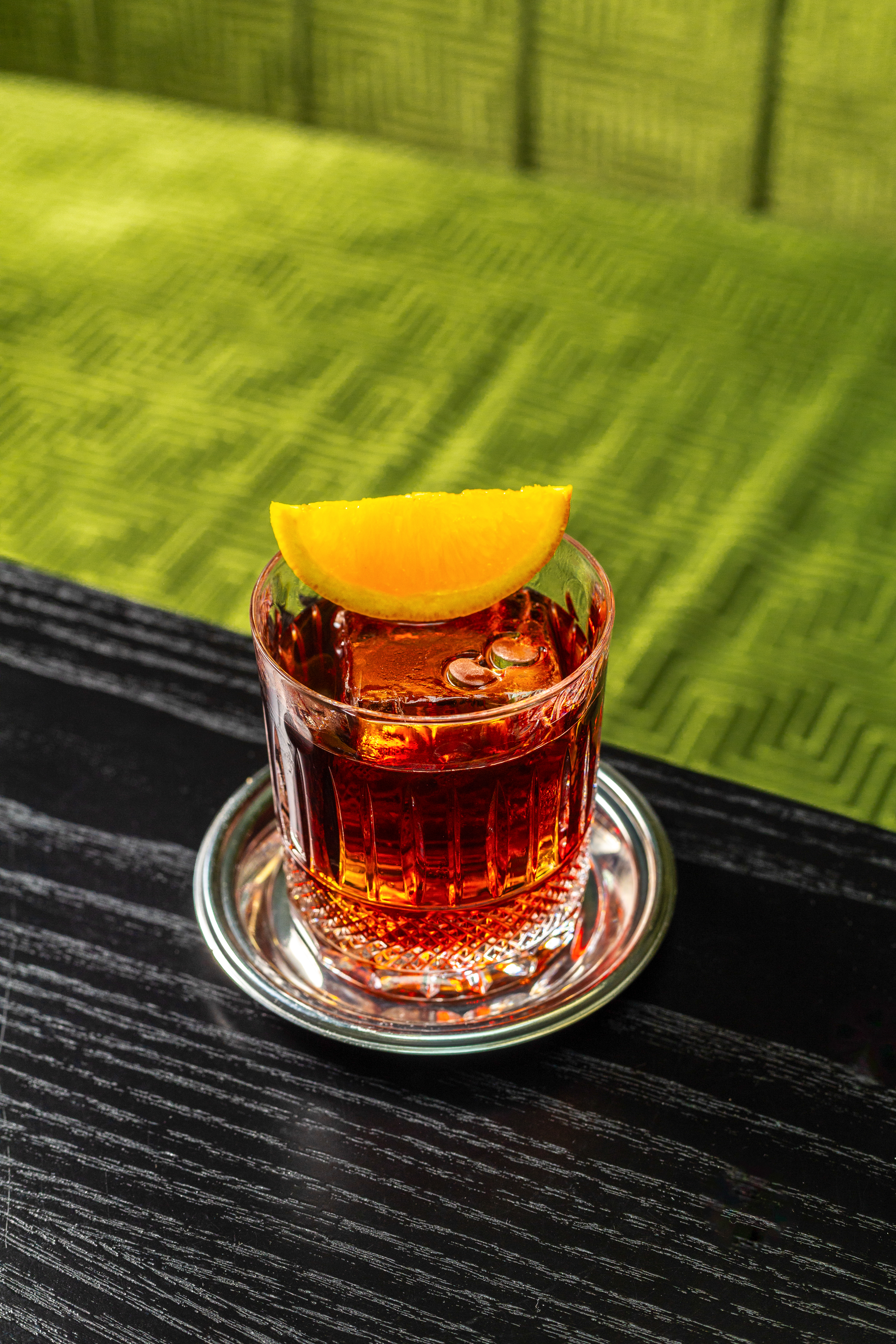 Amber cocktail with orange slice and ice in cut glass, dark wood table.