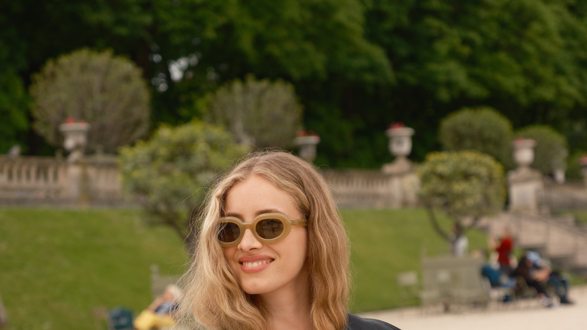a woman wearing sunglasses and a black coat holding a book