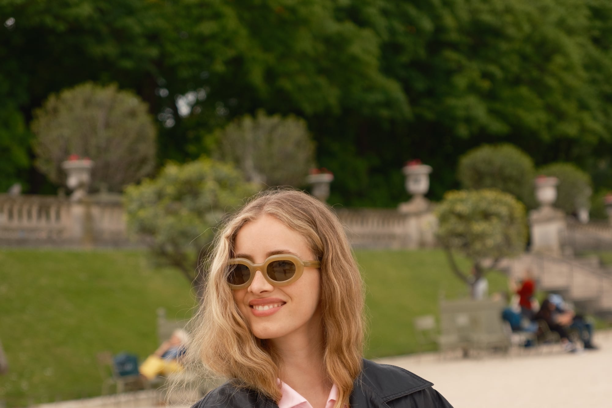 a woman wearing sunglasses and a black coat holding a book