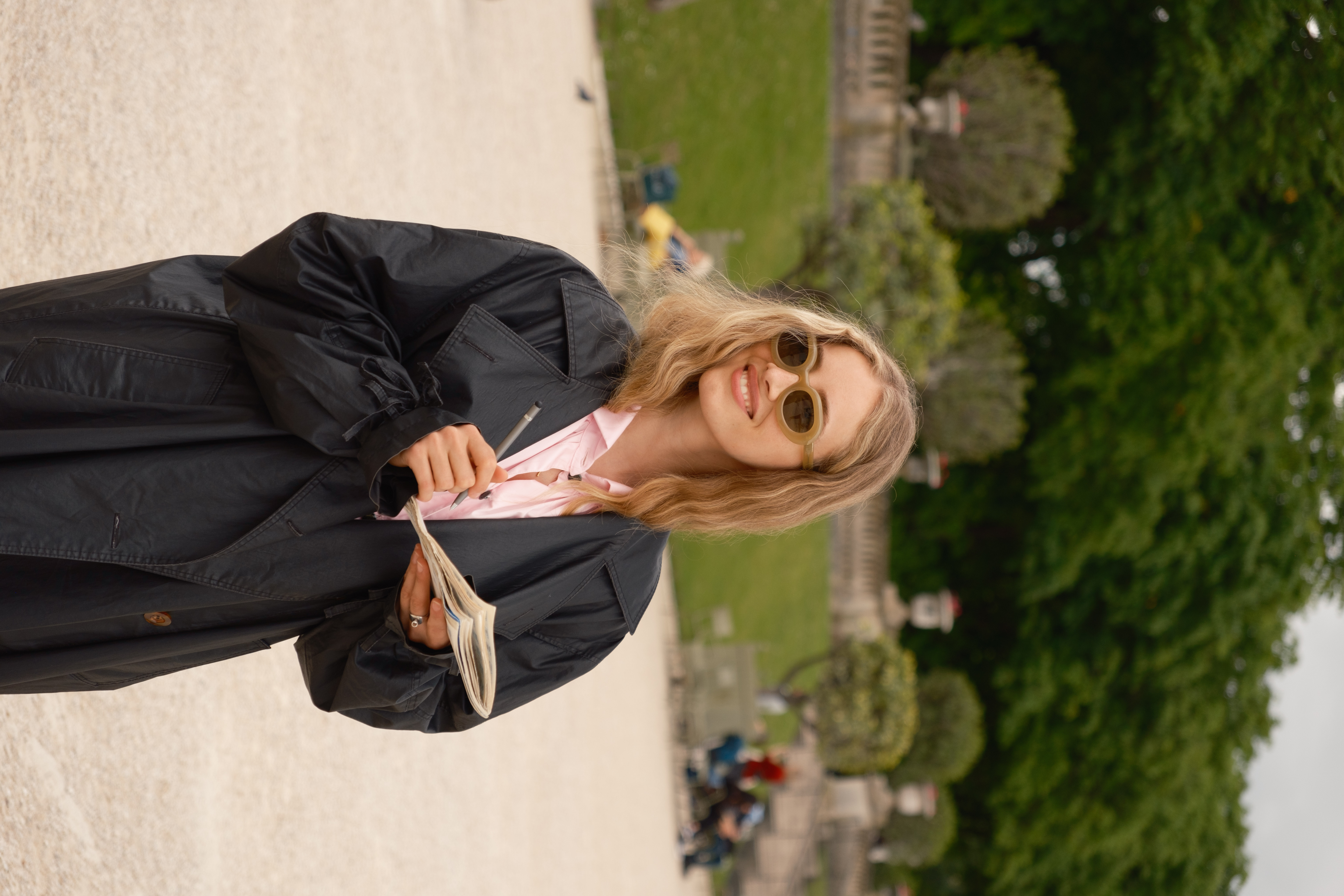 a woman wearing sunglasses and a black coat holding a book