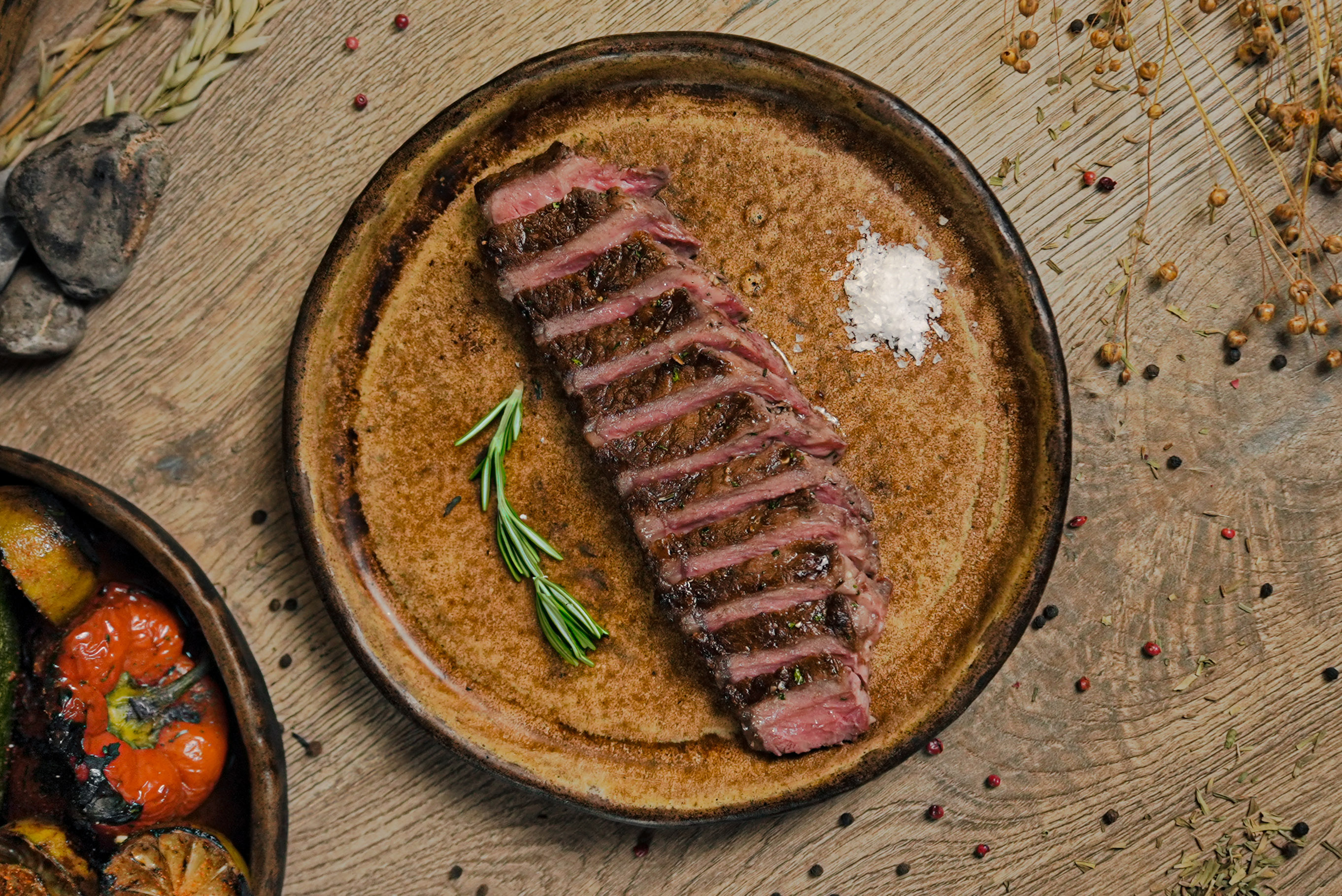 Sliced medium-rare steak with rosemary, sea salt on a textured plate.