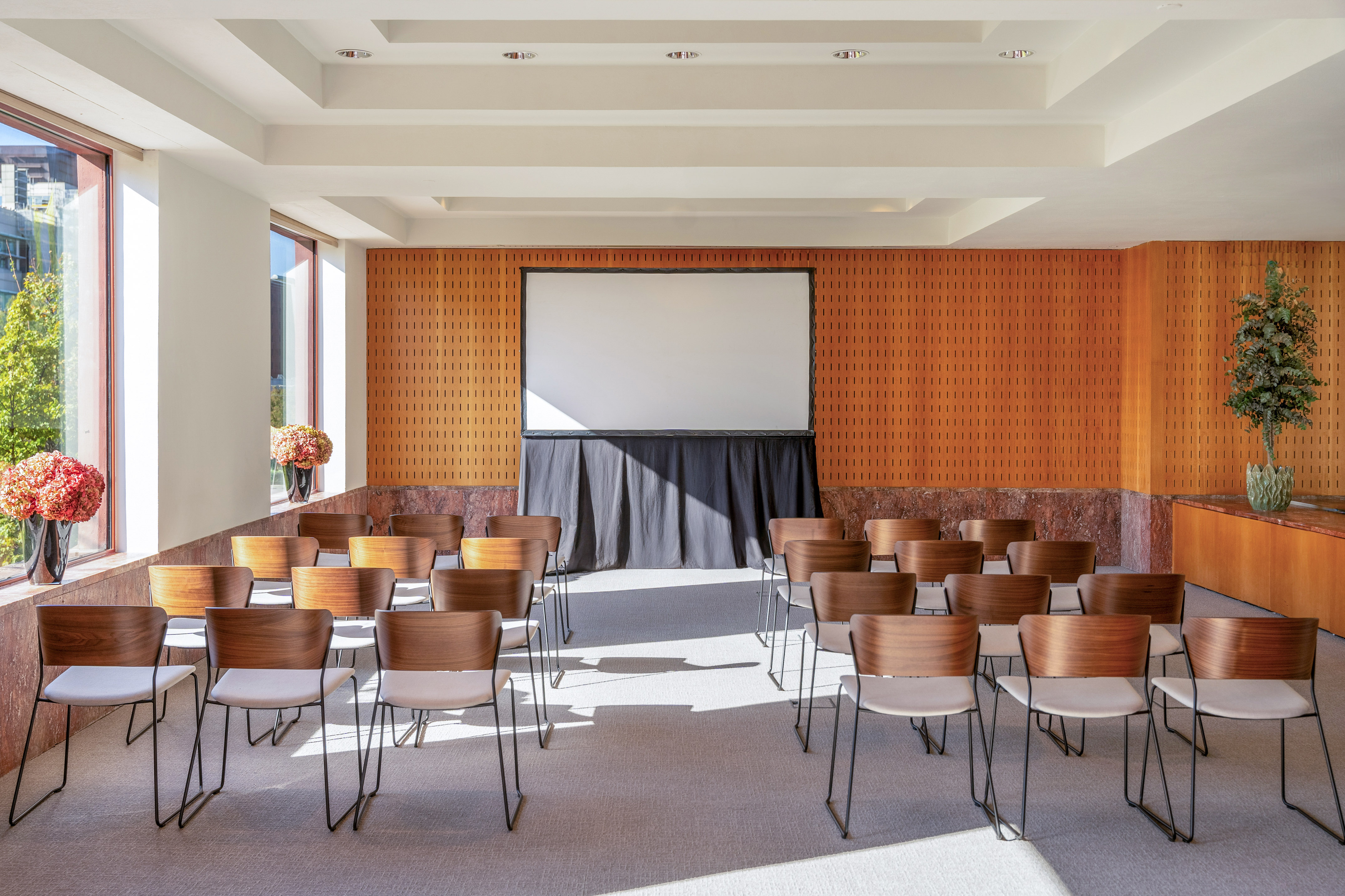 Bright modern meeting room with wooden chairs and a large projection screen.
