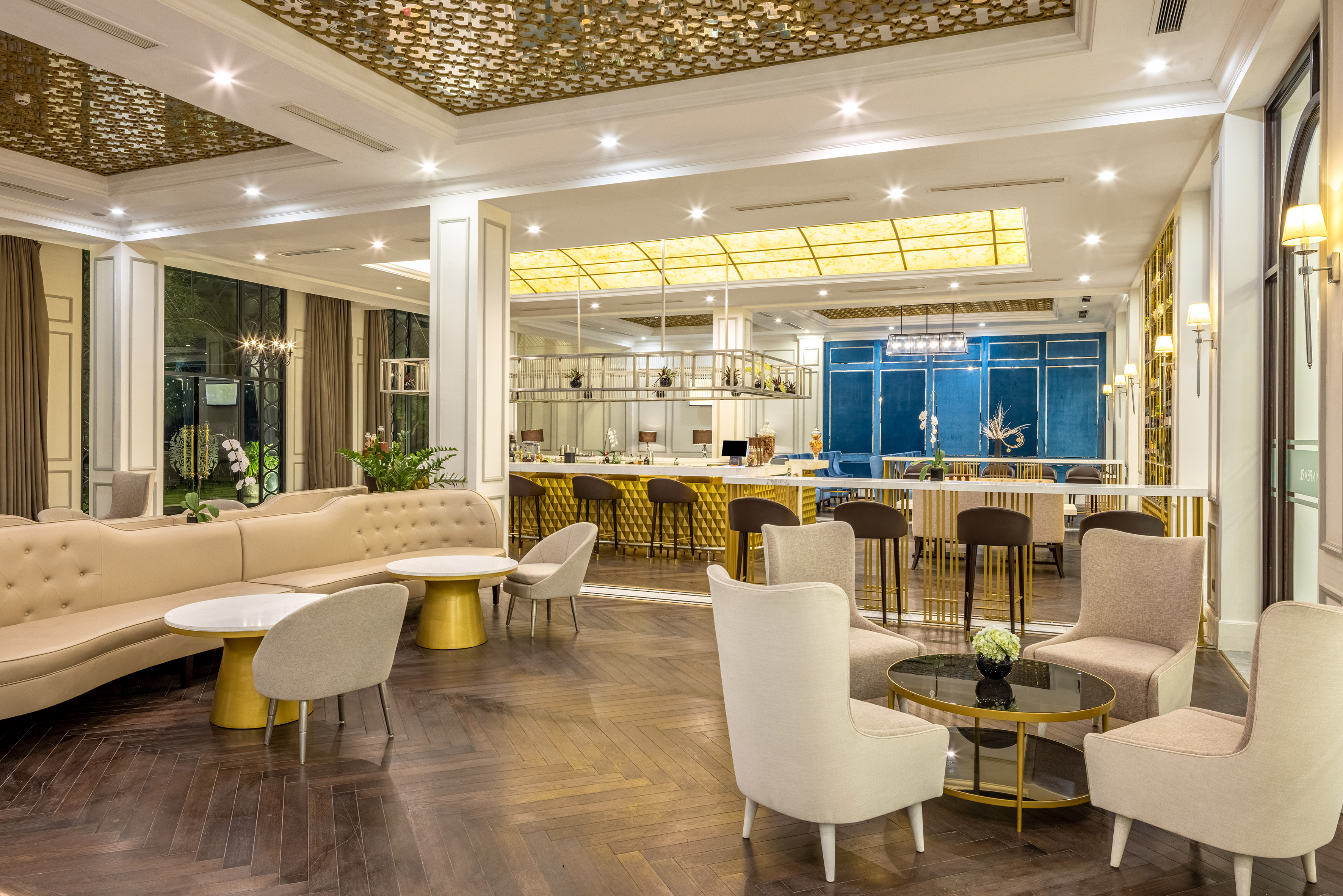 Modern luxury hotel lobby lounge with bar, beige seating, and dark wood floor.