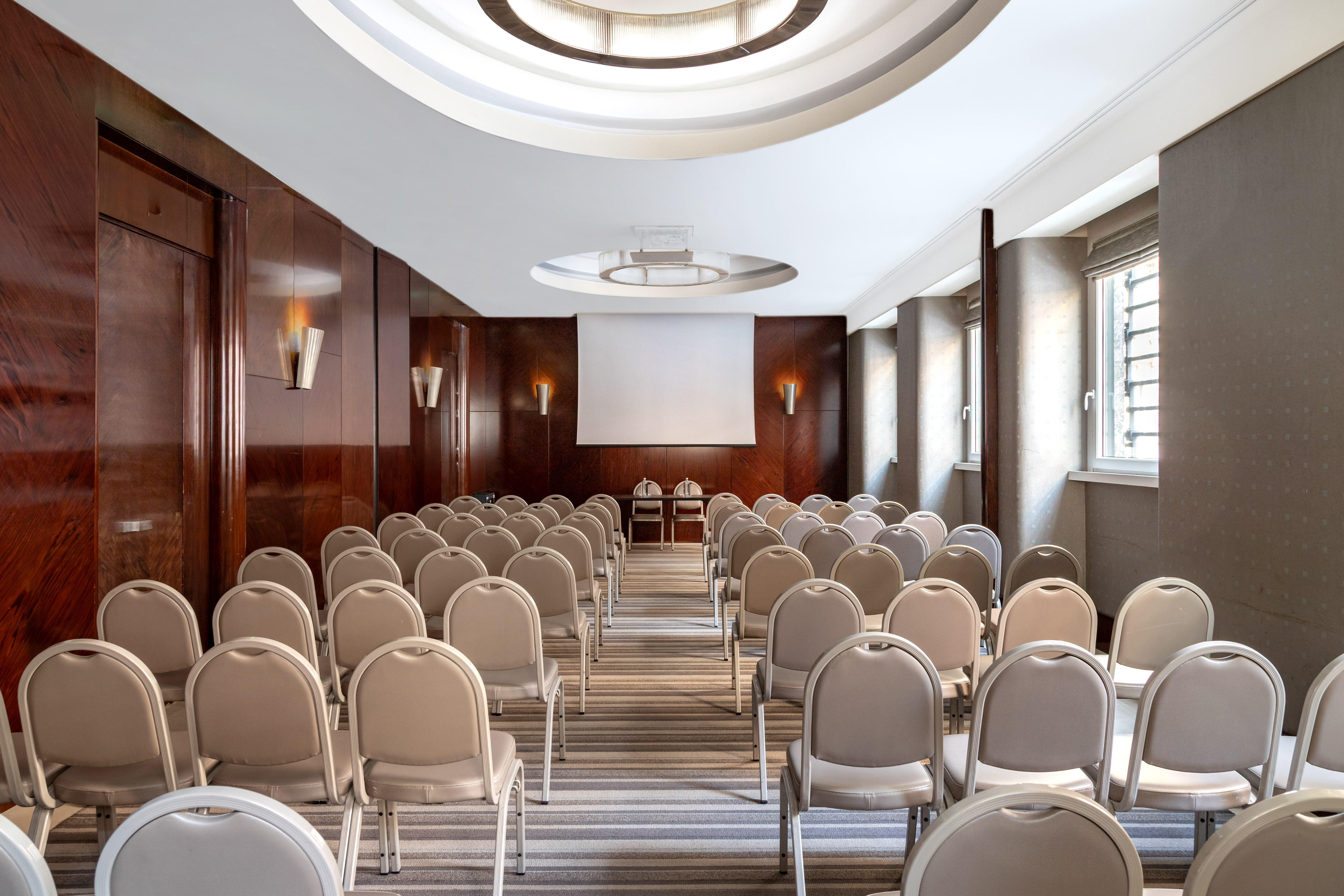 Empty meeting room with projector screen, rows of chairs, and wood paneling. - Madreperla 2 - Meliá Genova, Genua