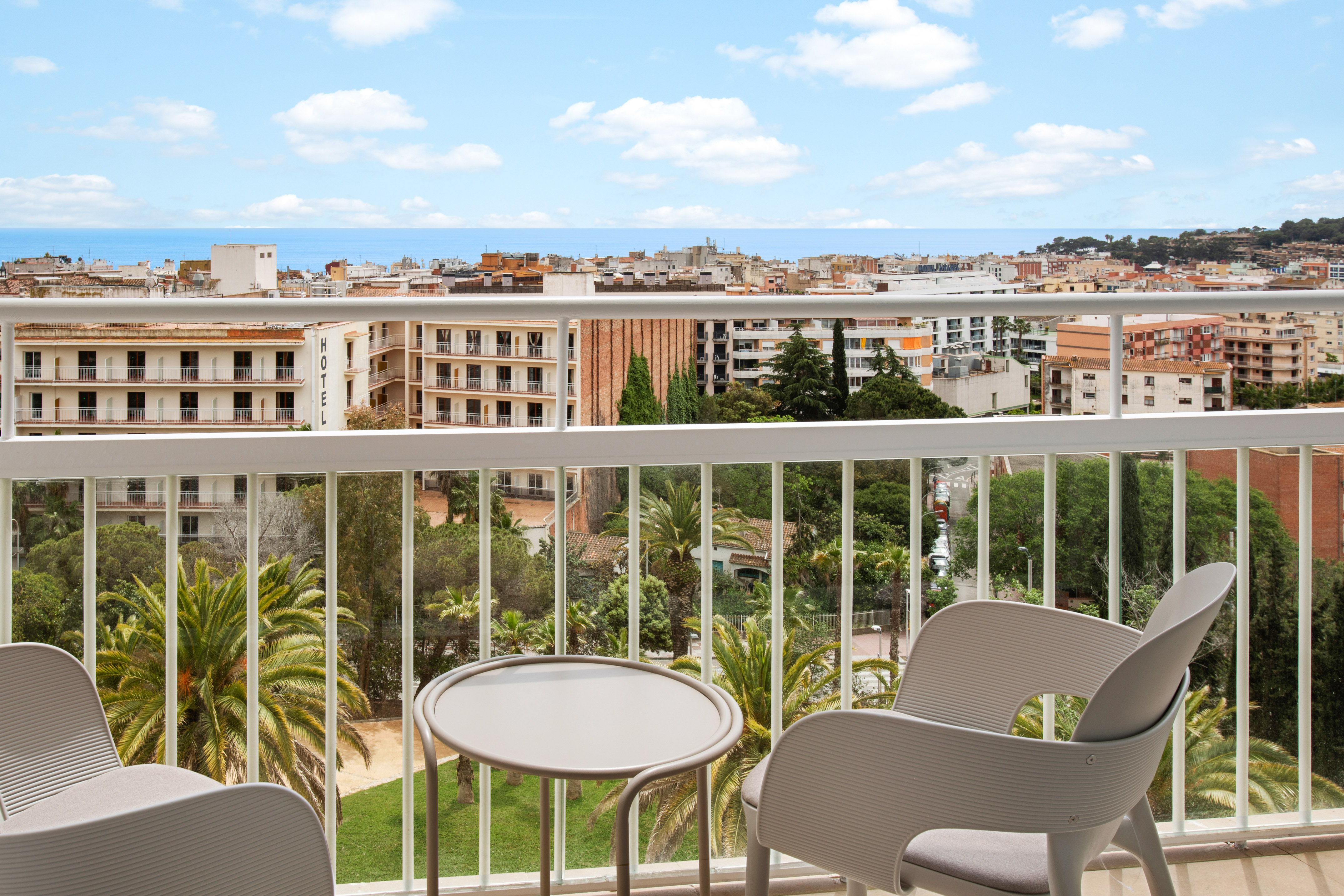 Hotel balcony with chairs, table, city, and distant sea view.