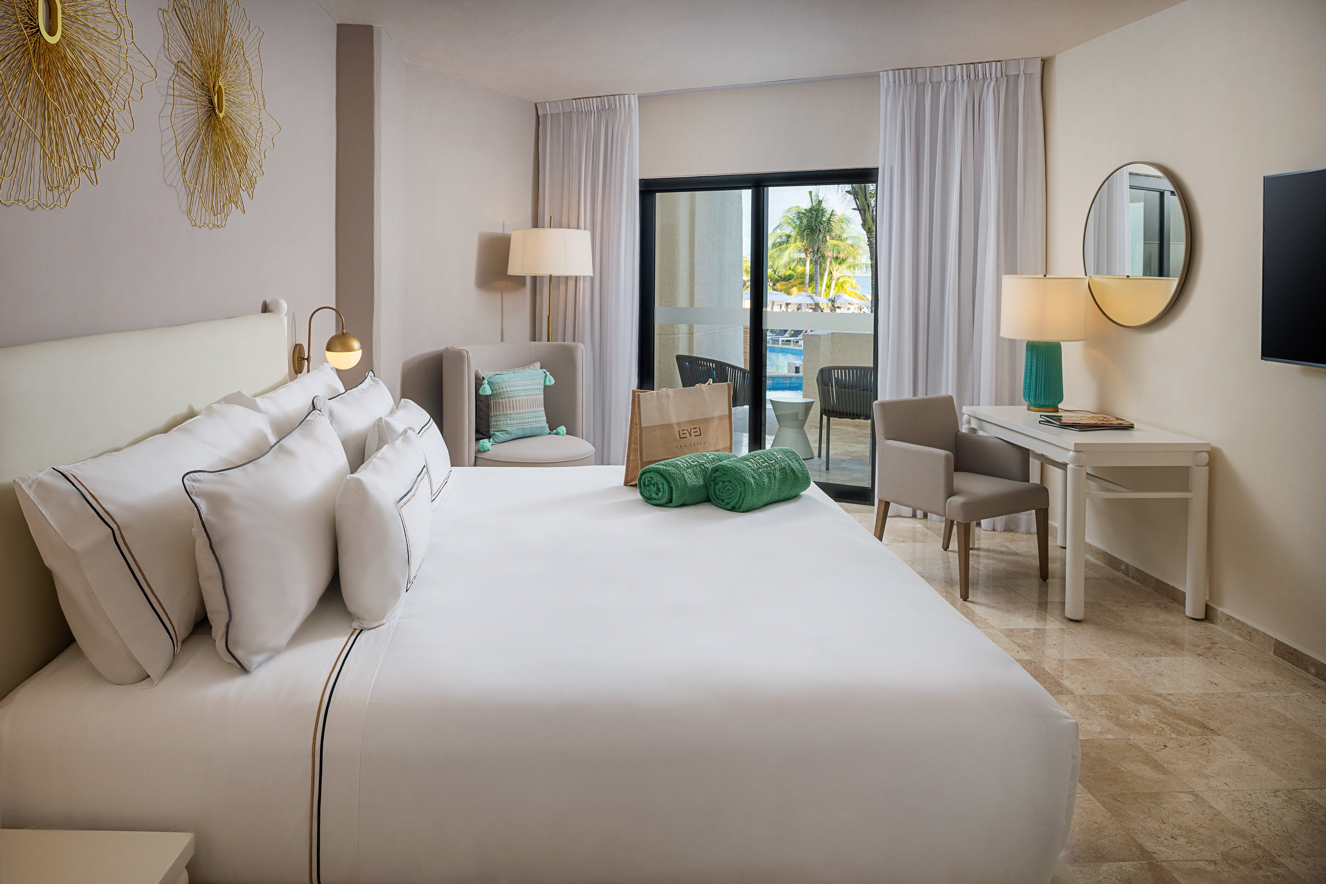 Modern hotel room with large bed, balcony pool view, desk, and elegant gold decor.