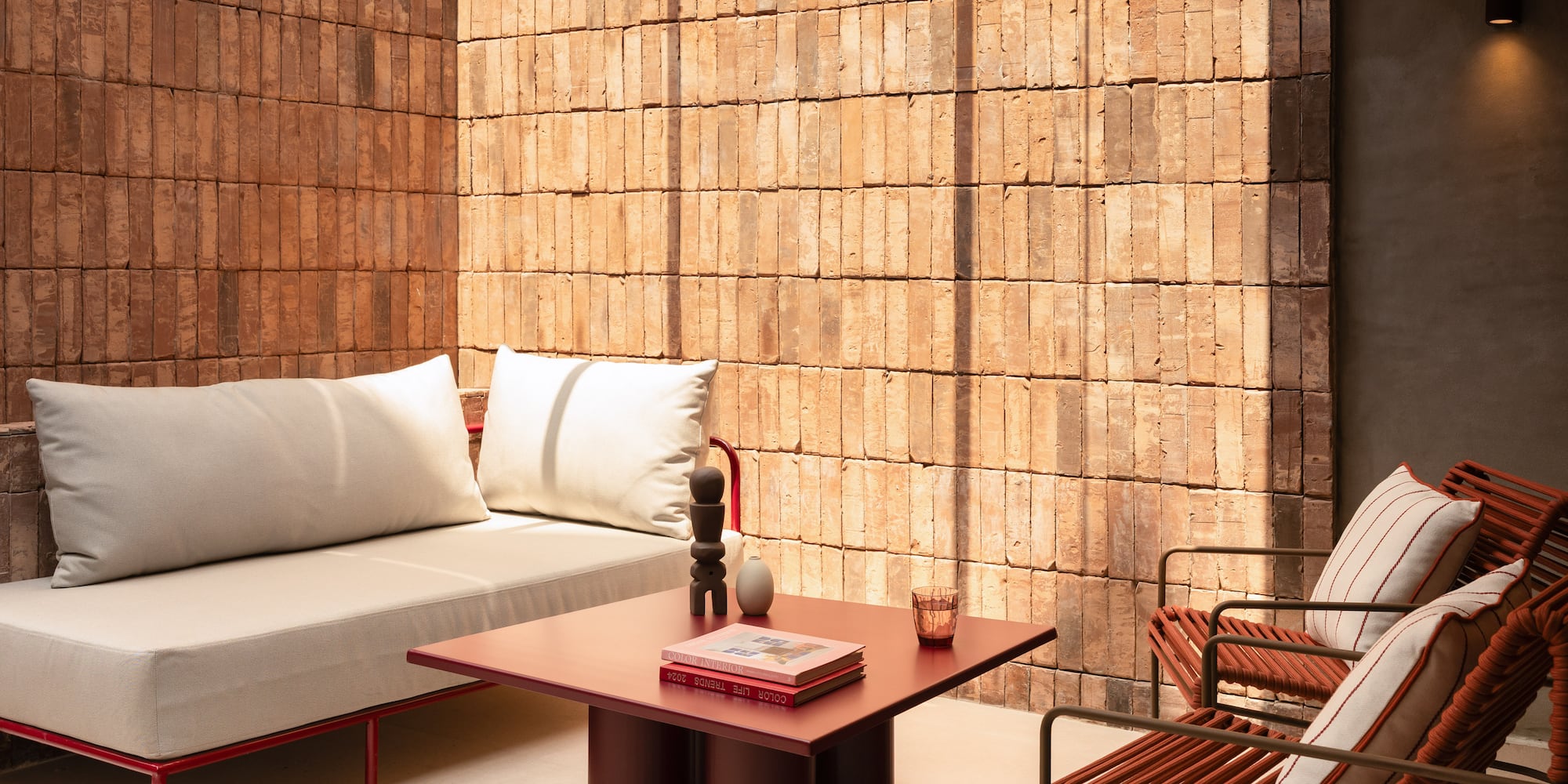 Modern patio furniture: red sofa, woven chairs, coffee table, brick wall.