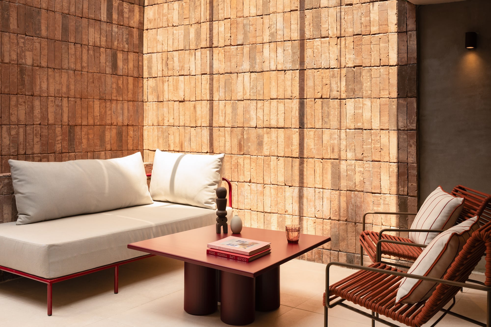 Modern patio furniture: red sofa, woven chairs, coffee table, brick wall.