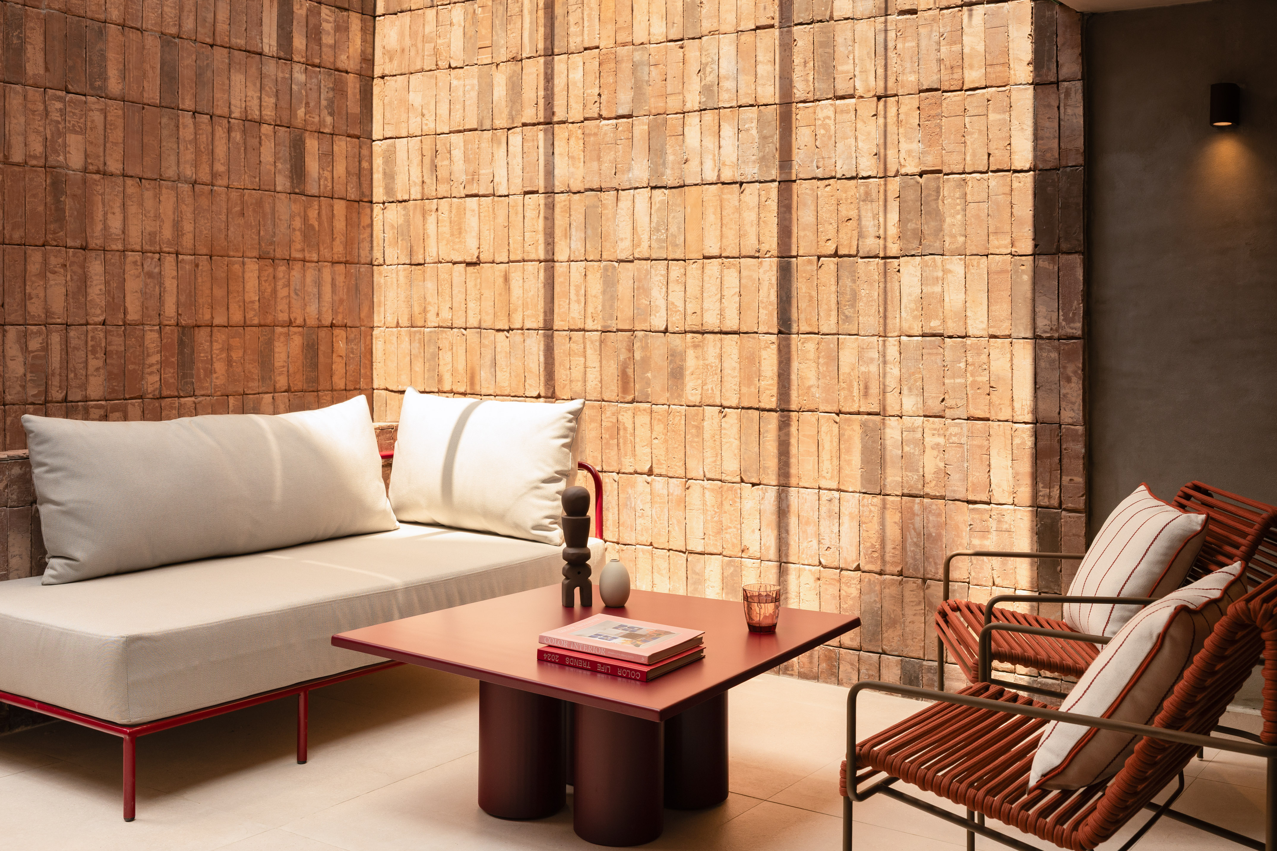 Modern patio furniture: red sofa, woven chairs, coffee table, brick wall.