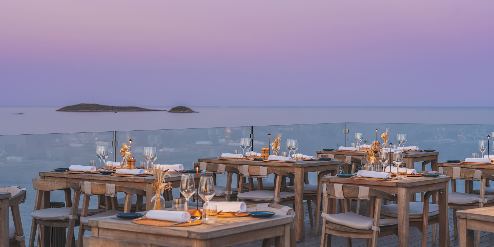 Outdoor dining terrace with wooden tables overlooking the ocean at sunset.