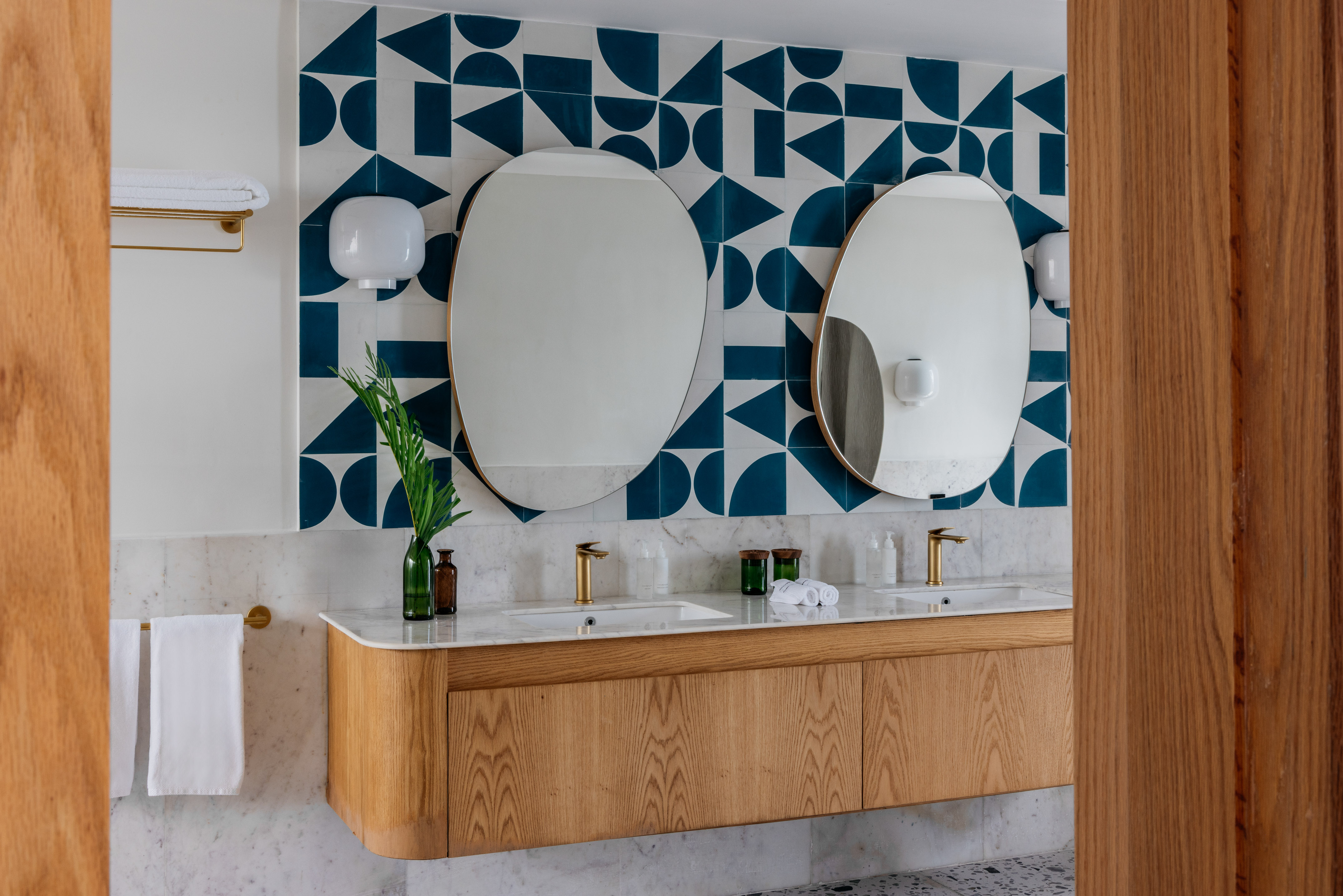 Modern double vanity, wood cabinet, marble counter, gold faucets, blue geometric tiles.
