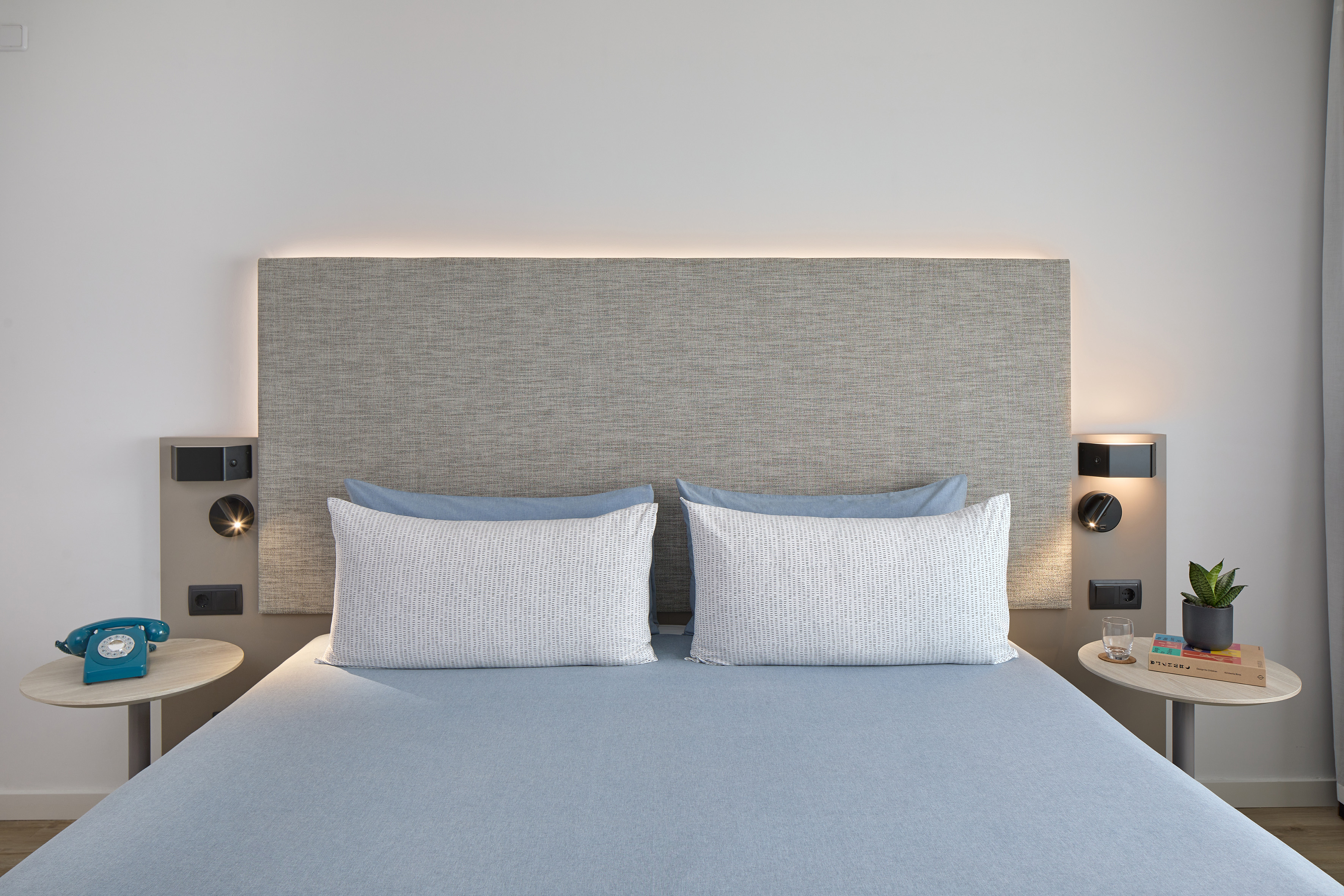 Contemporary hotel room with blue bed, gray headboard, and sleek bedside tables.
