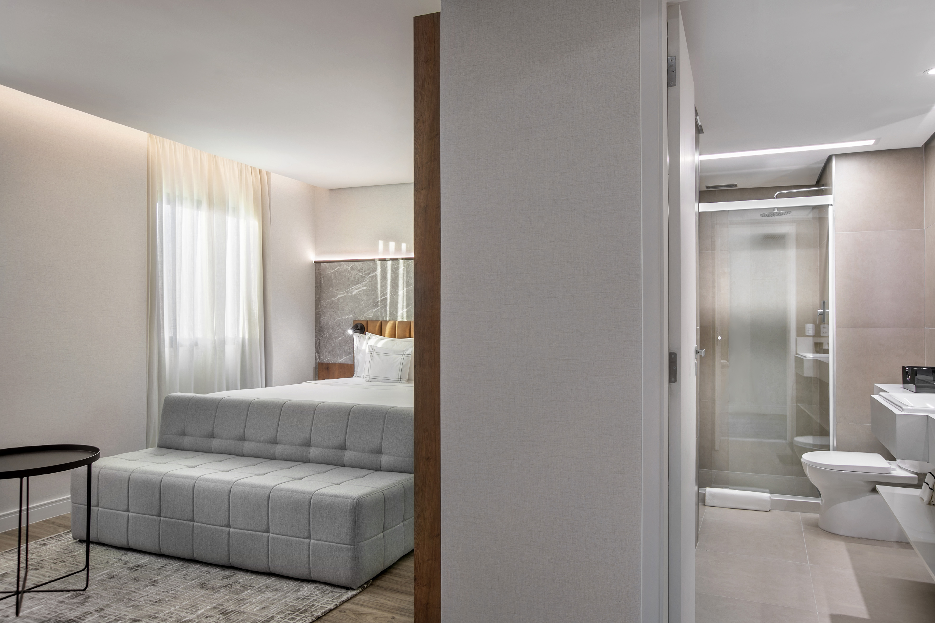 Modern hotel room with bed, gray modular sofa, and ensuite bathroom.
