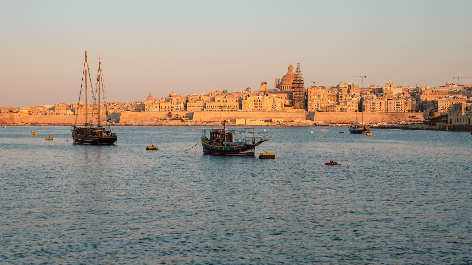 Valletta, Malta cityscape at sunset with historic buildings and boats in the harbor.