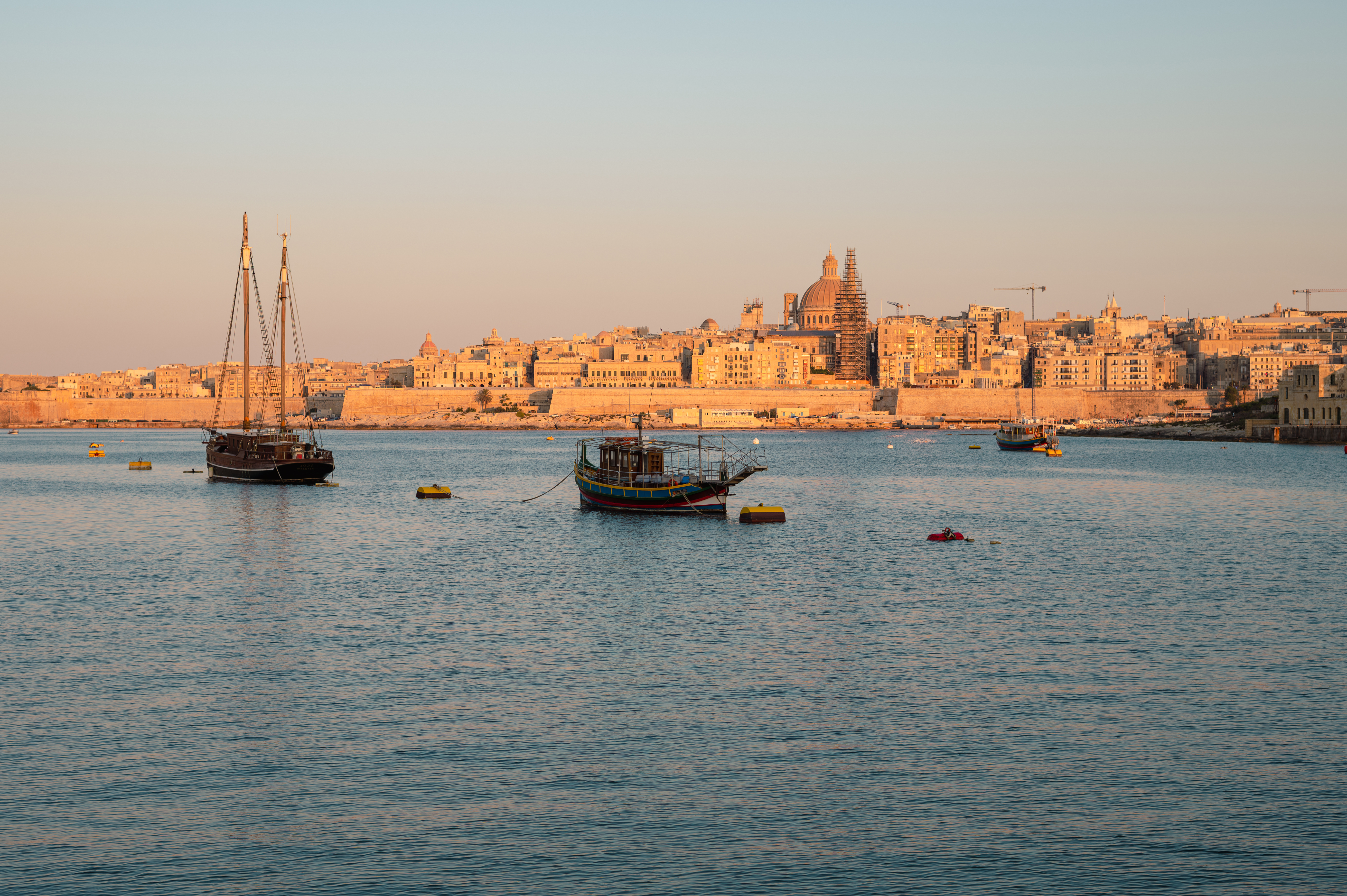 Valletta, Malta cityscape at sunset with historic buildings and boats in the harbor.