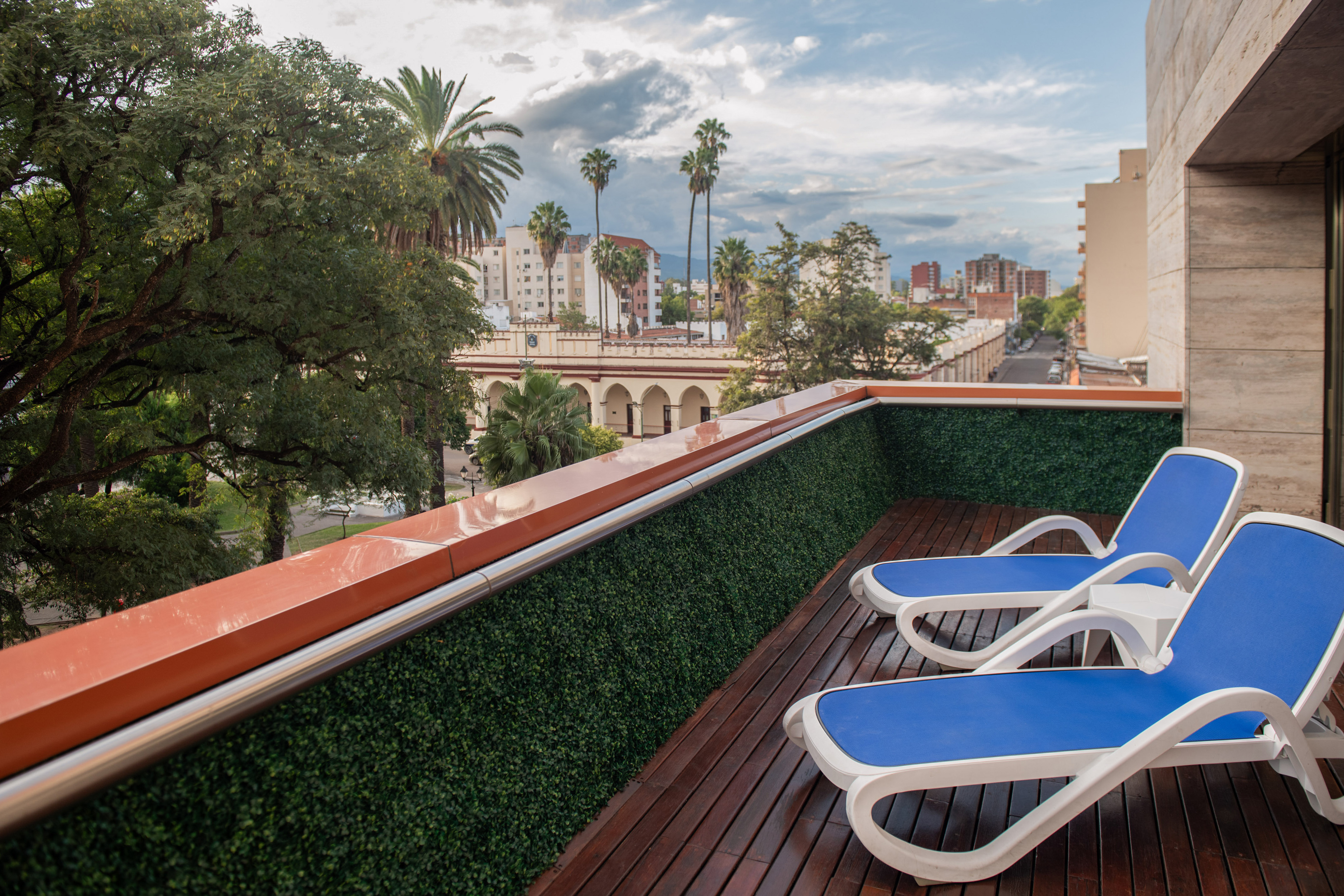 Balcony with lounge chairs, wooden deck, green wall, and city skyline.