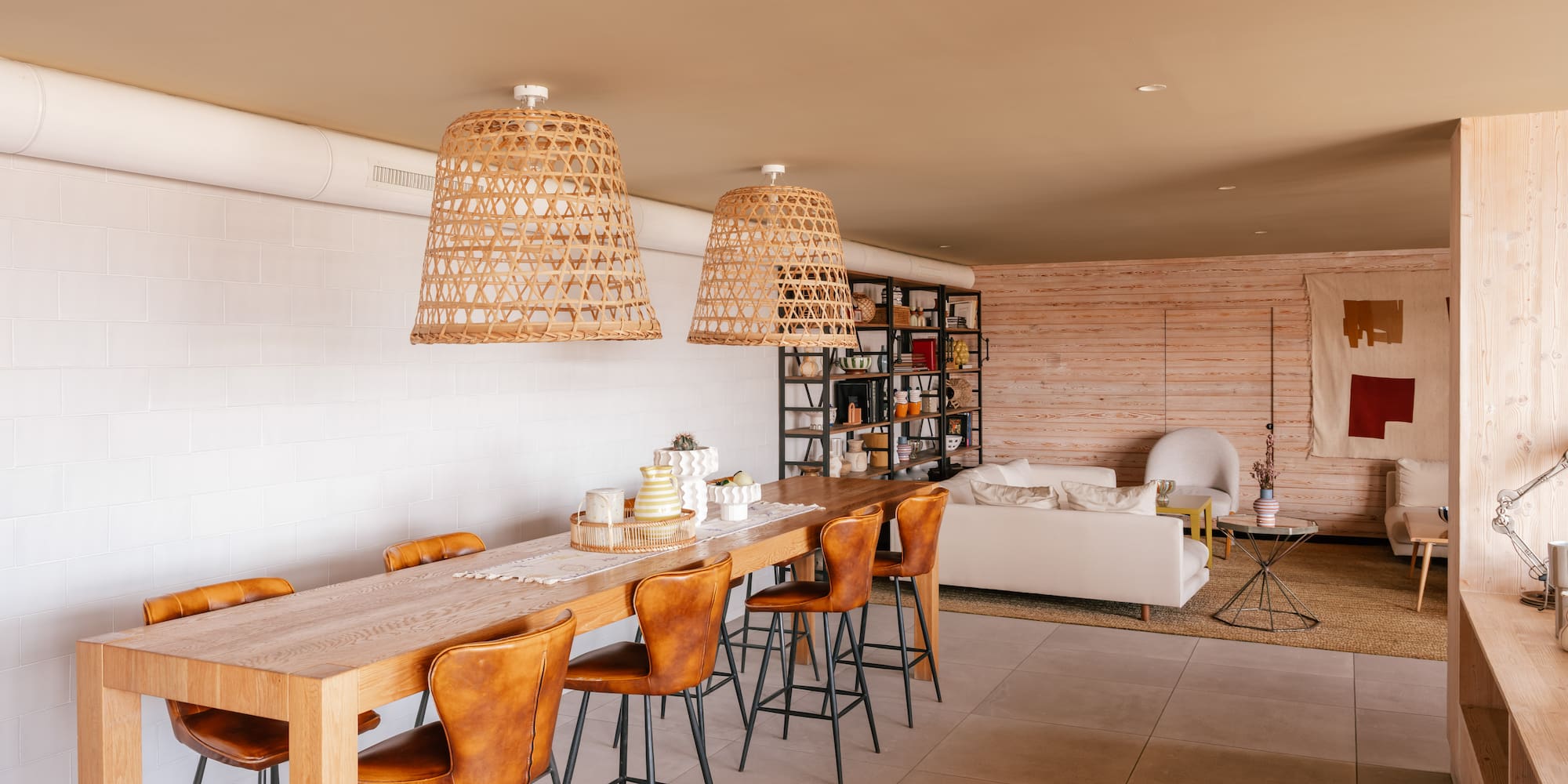 Open dining and living room with wood table, leather stools, rattan lights.