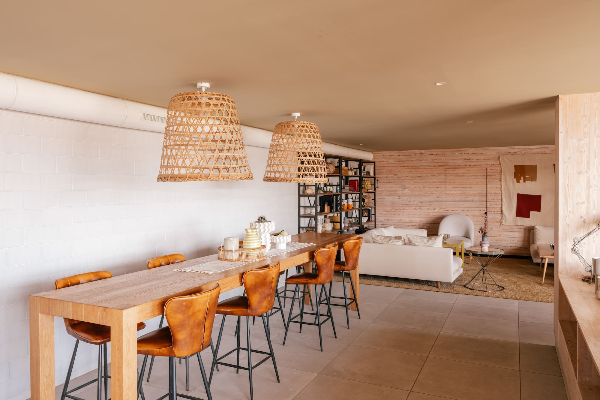 Open dining and living room with wood table, leather stools, rattan lights.