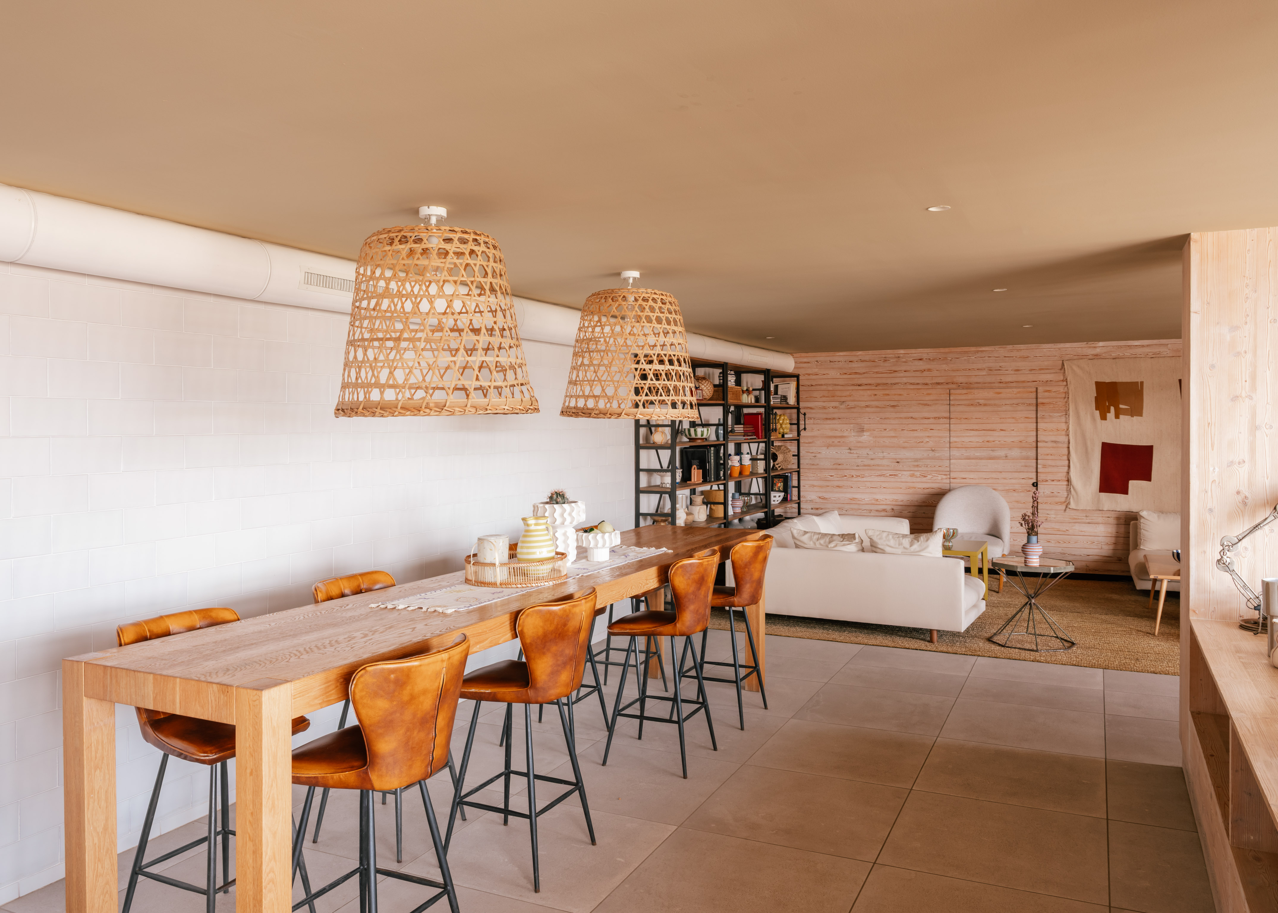 Open dining and living room with wood table, leather stools, rattan lights.