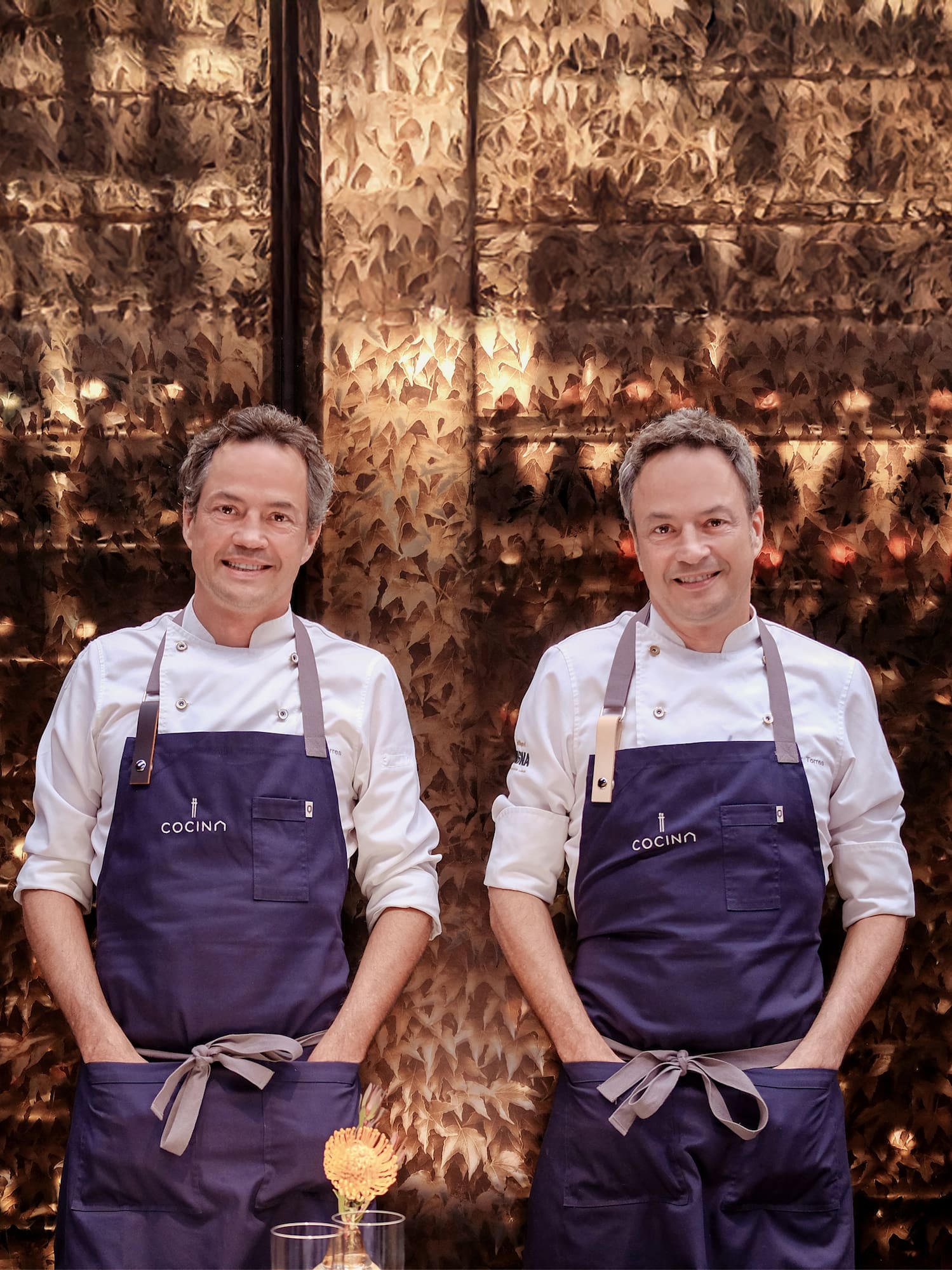 two men wearing aprons standing in front of a wall