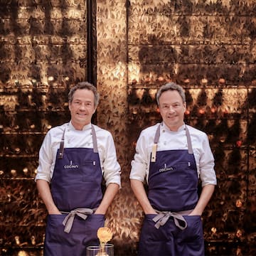 two men wearing aprons standing in front of a wall