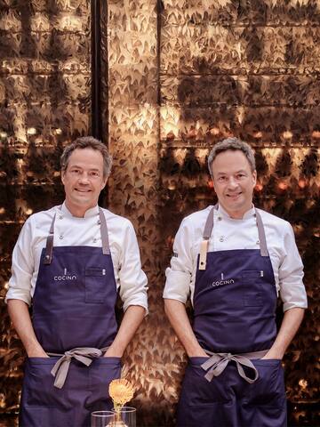 two men wearing aprons standing in front of a wall