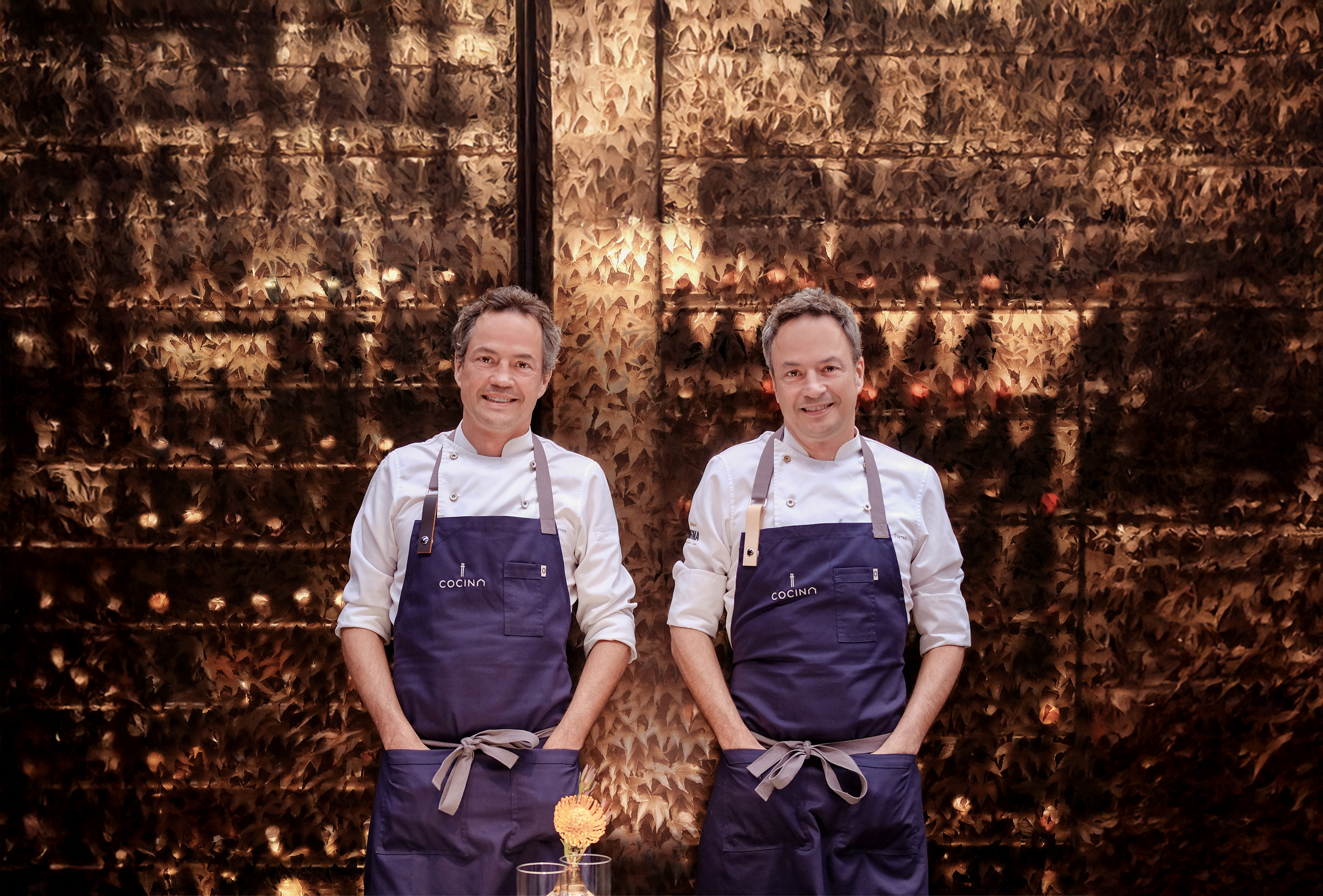 two men wearing aprons standing in front of a wall