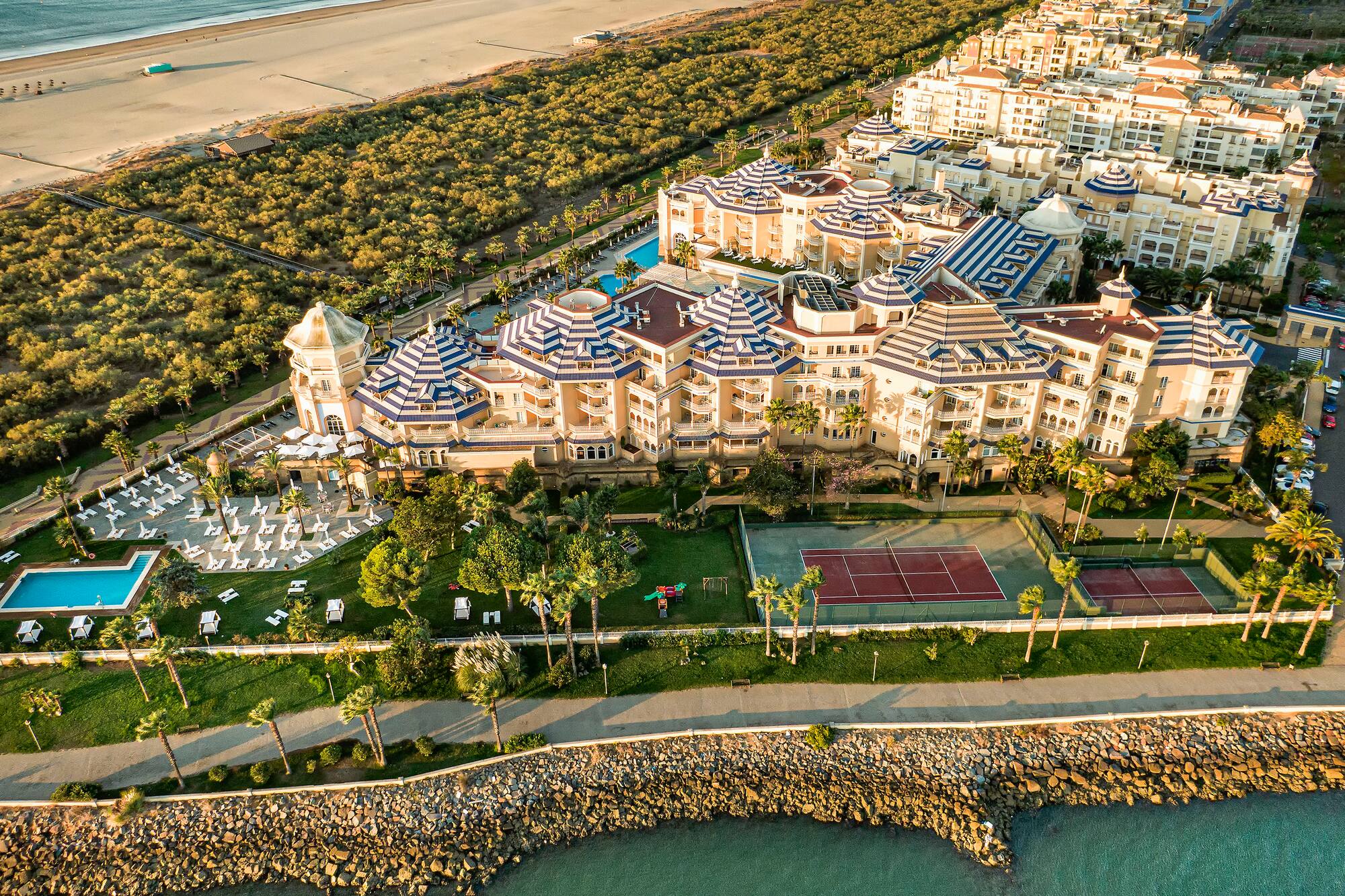 Aerial view: luxury coastal resort with beach, ocean, pools, and tennis courts.
