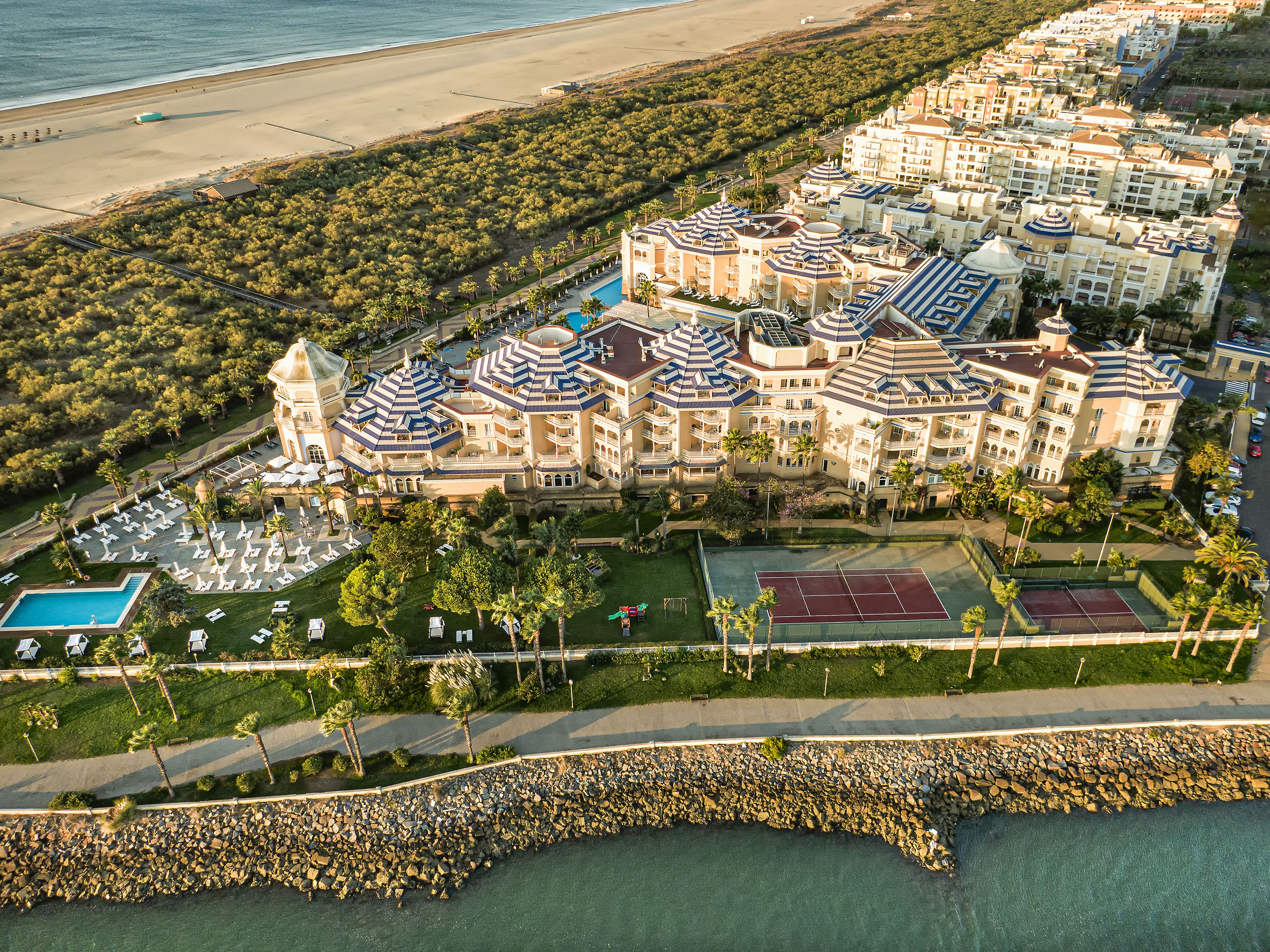 Aerial view: luxury coastal resort with beach, ocean, pools, and tennis courts.