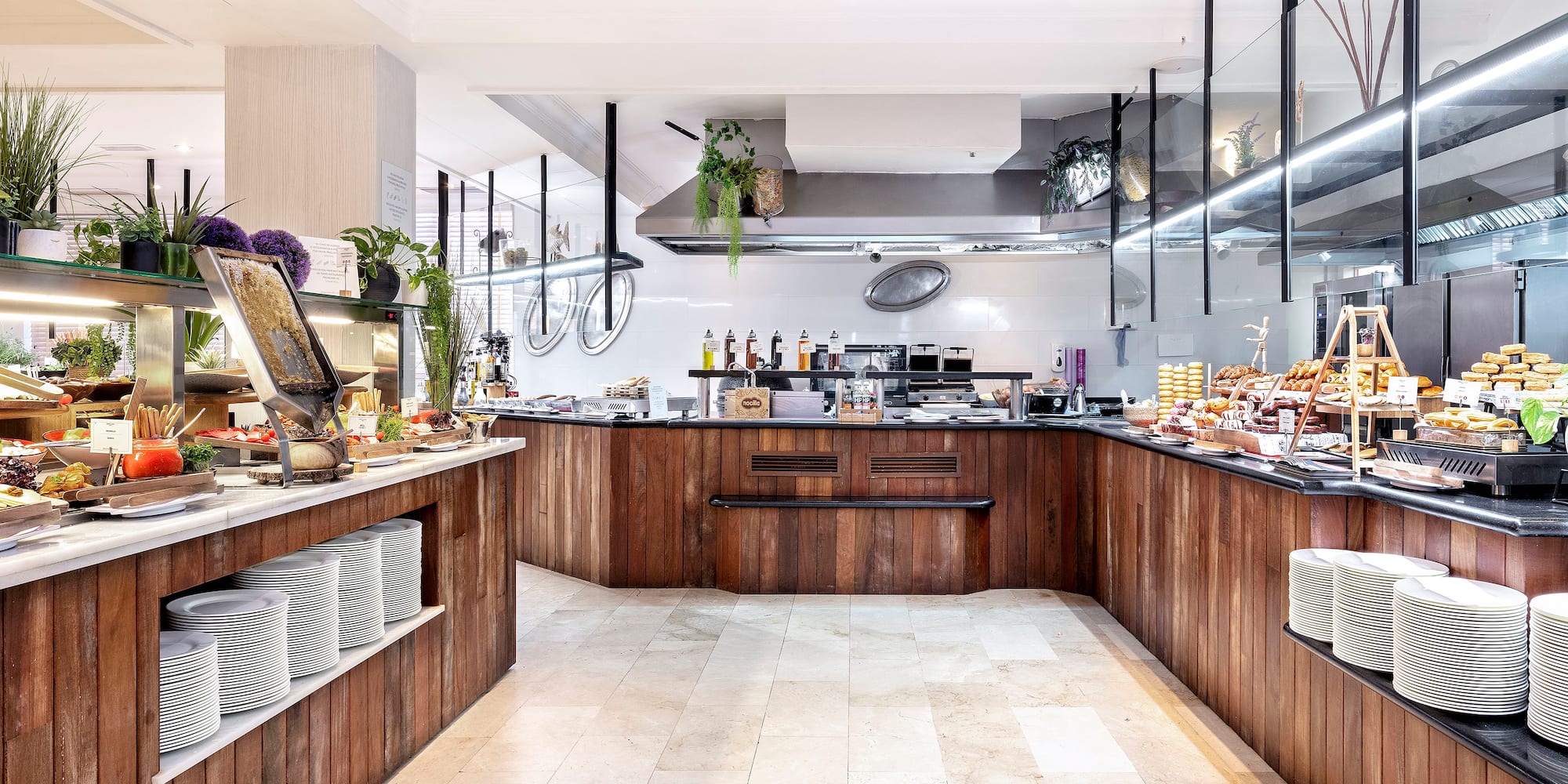 Hotel breakfast buffet with food stations, wooden counters, and kitchen.
