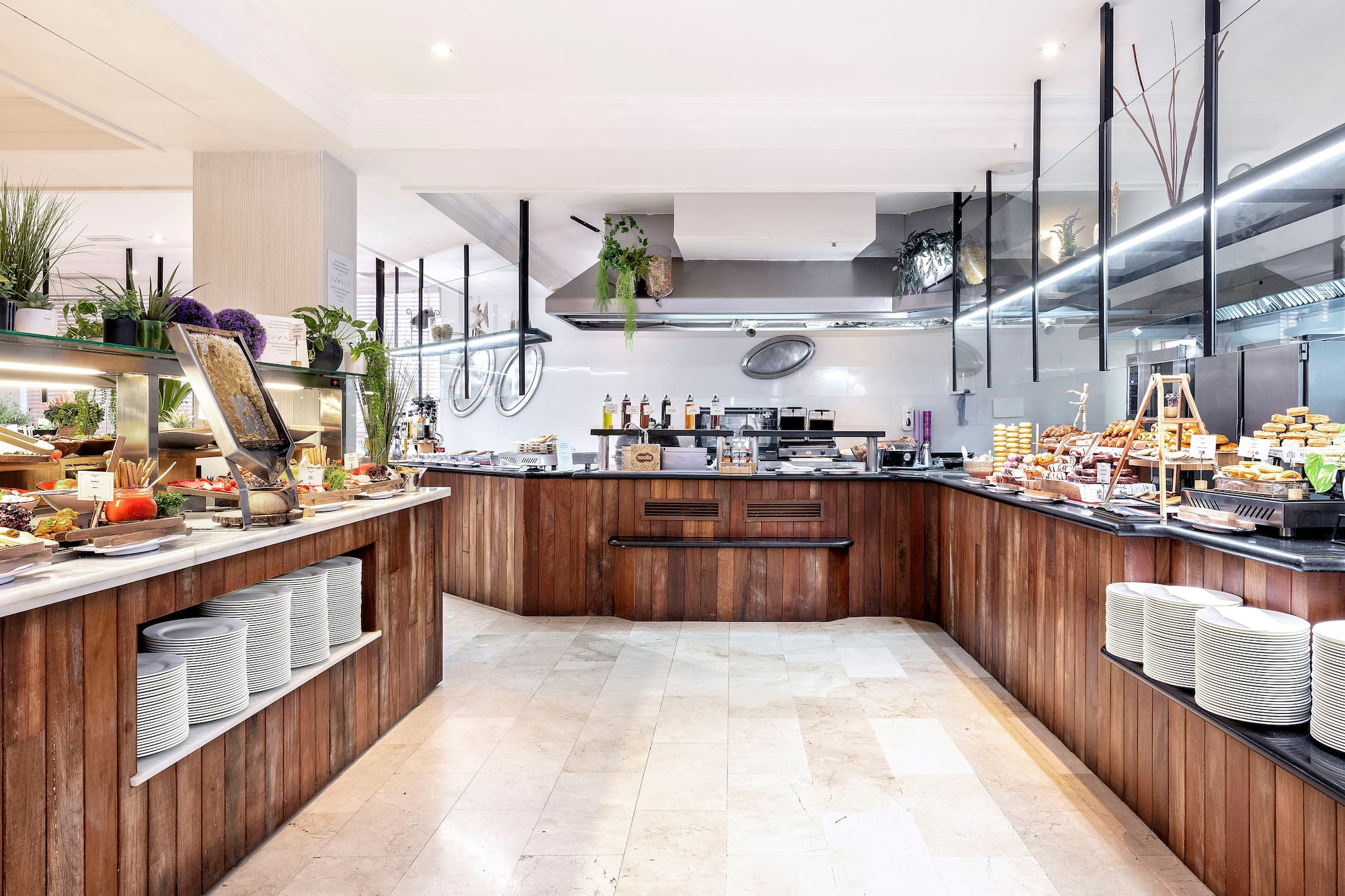 Hotel breakfast buffet with food stations, wooden counters, and kitchen.