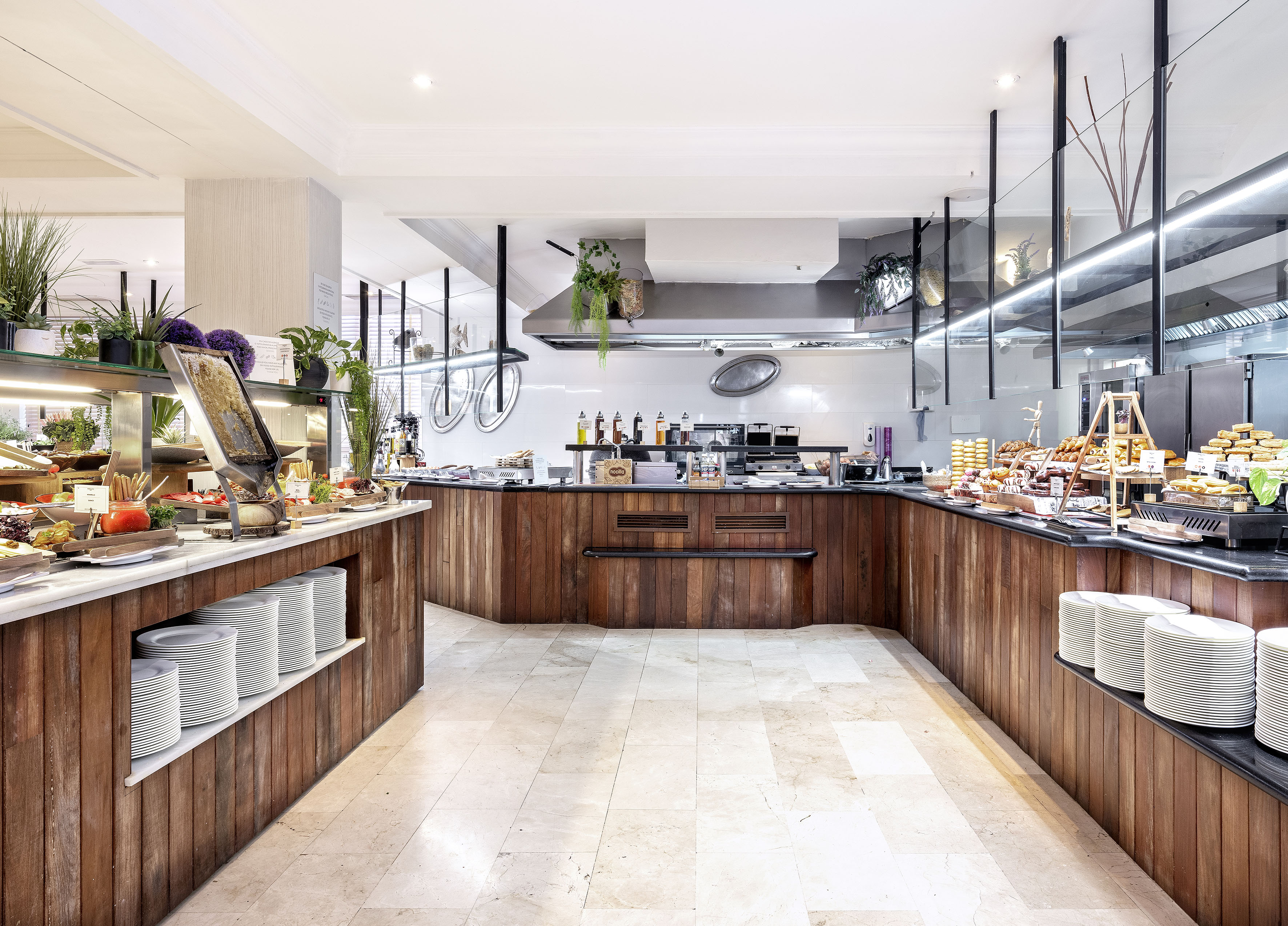 Hotel breakfast buffet with food stations, wooden counters, and kitchen.