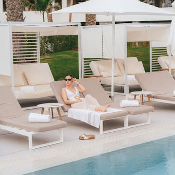a woman sitting in a lounge chair by a pool