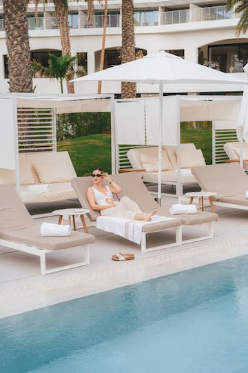 a woman sitting in a lounge chair by a pool