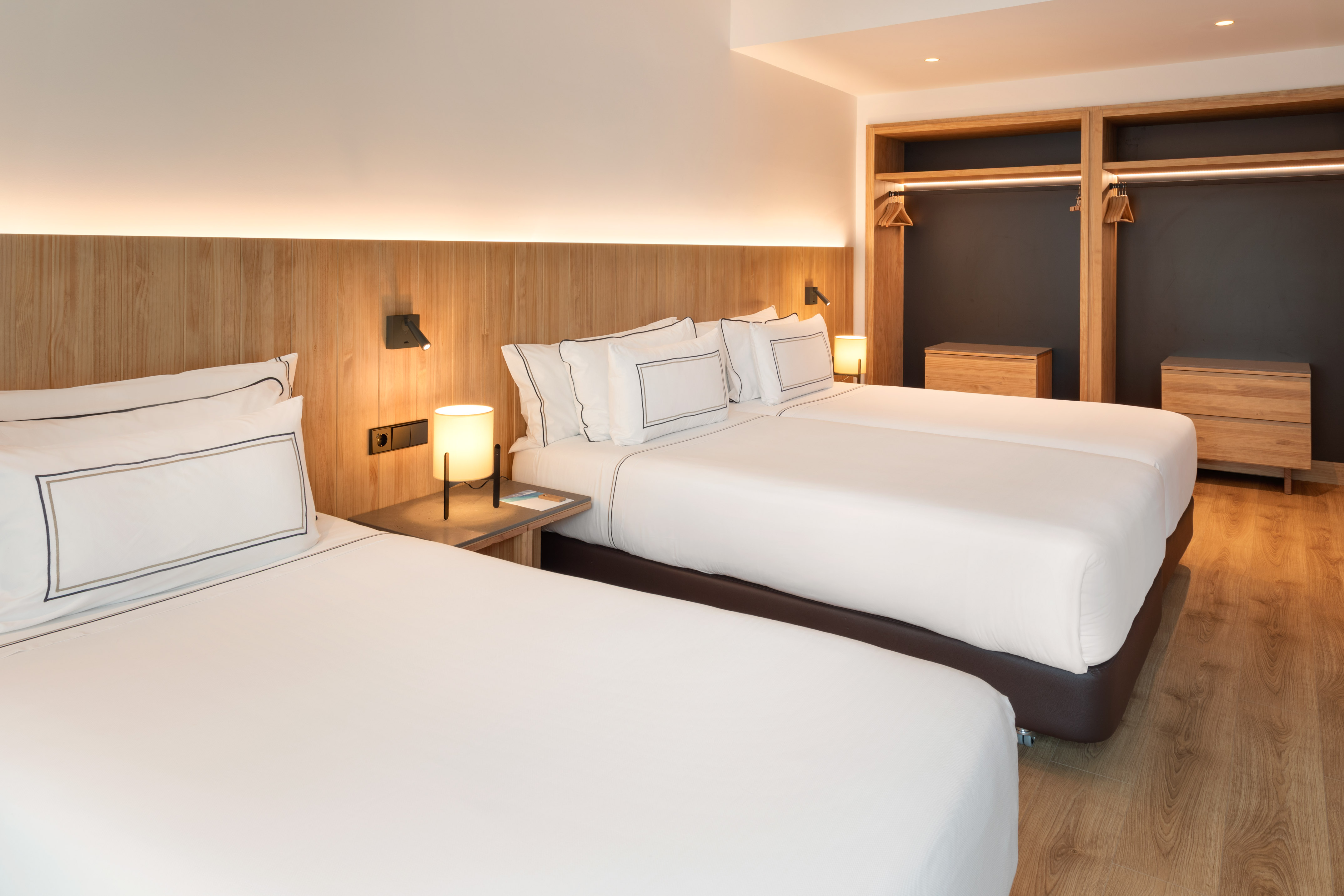 Modern hotel room with twin beds, wooden headboards, and open wardrobe.