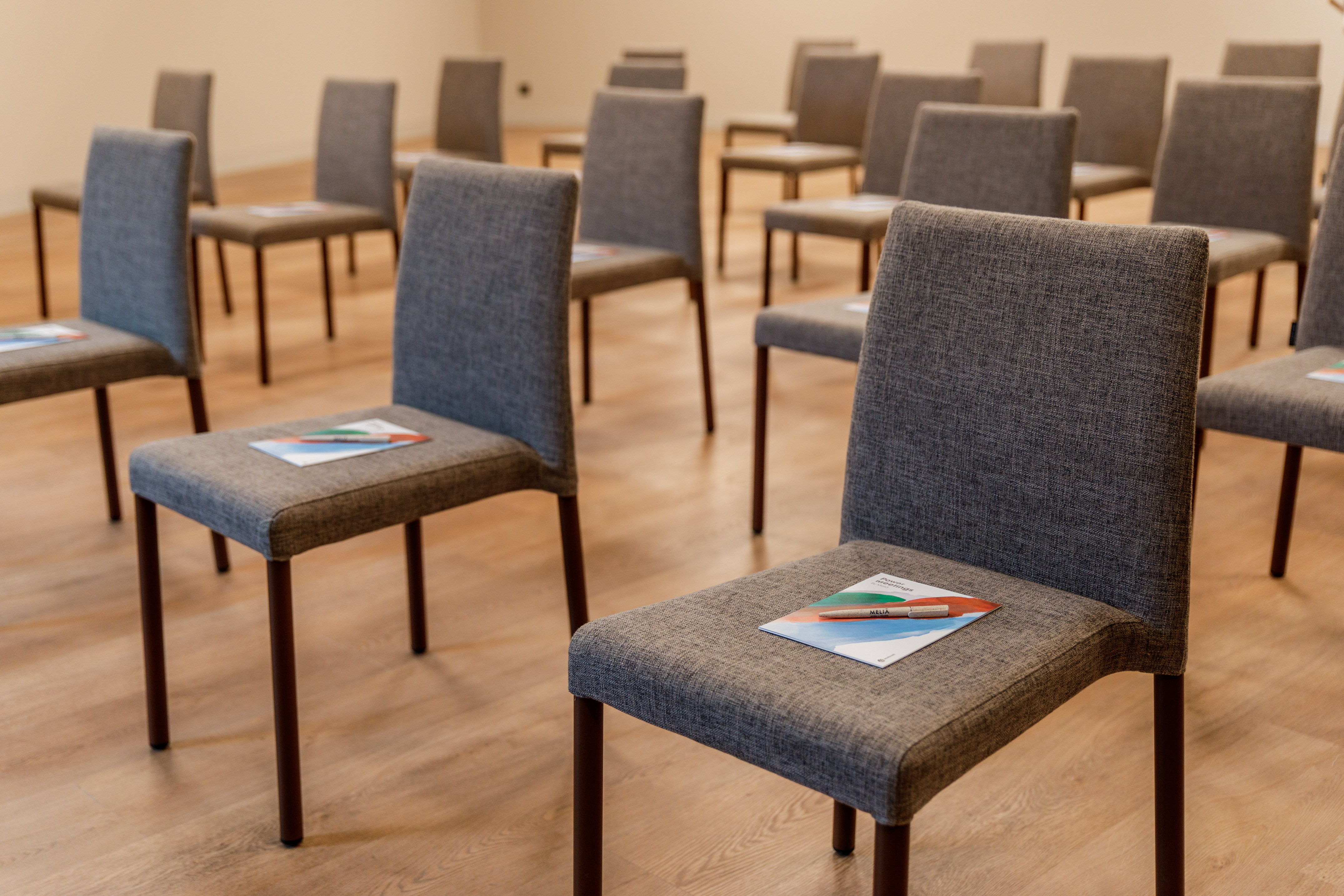 Conference room with rows of empty grey chairs and brochures.