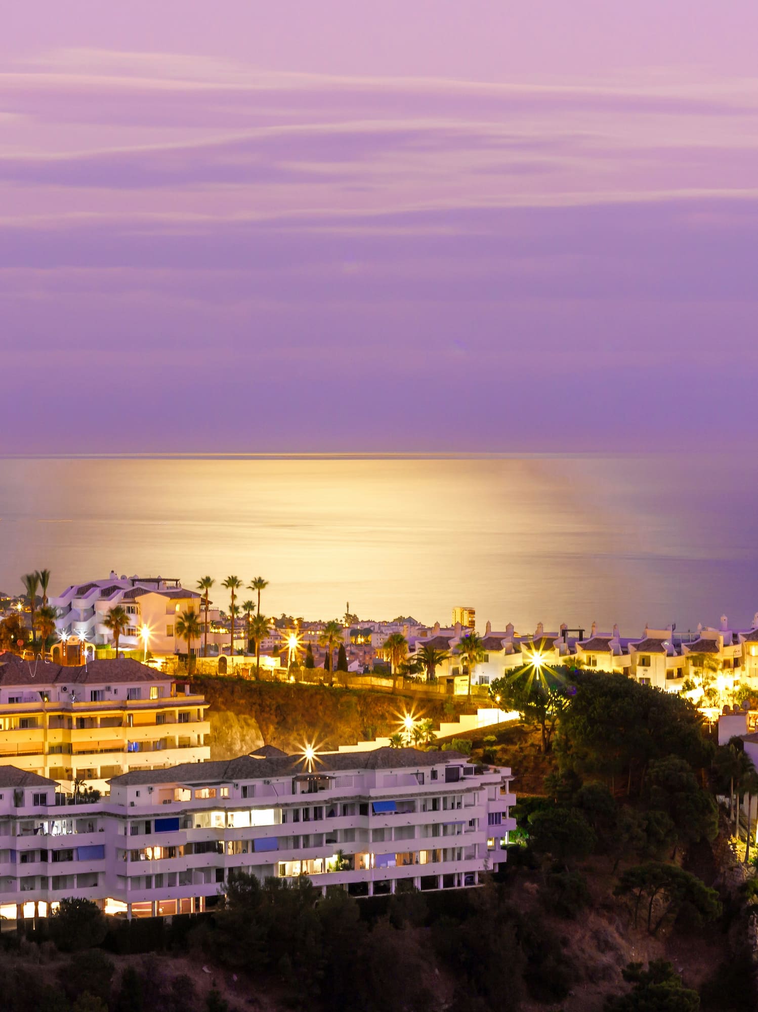 Illuminated coastal resort at twilight with palm trees and ocean view.