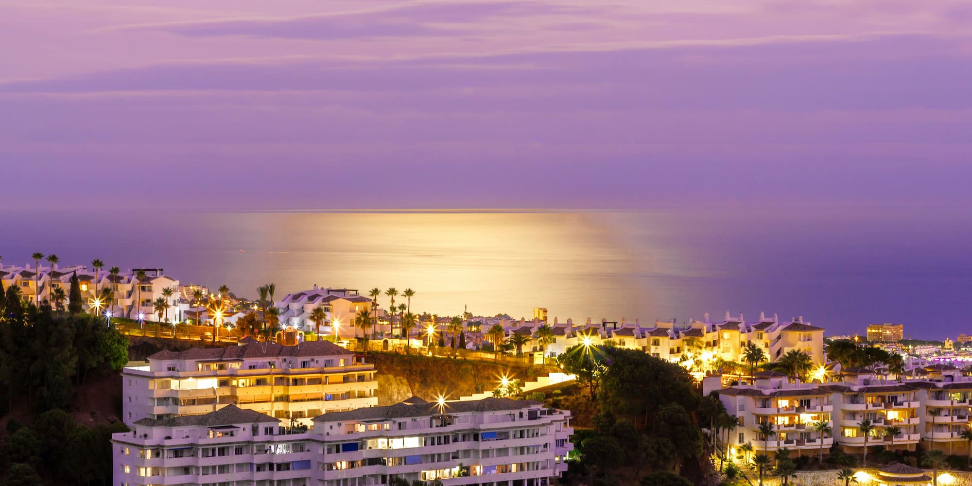Illuminated coastal resort at twilight with palm trees and ocean view.