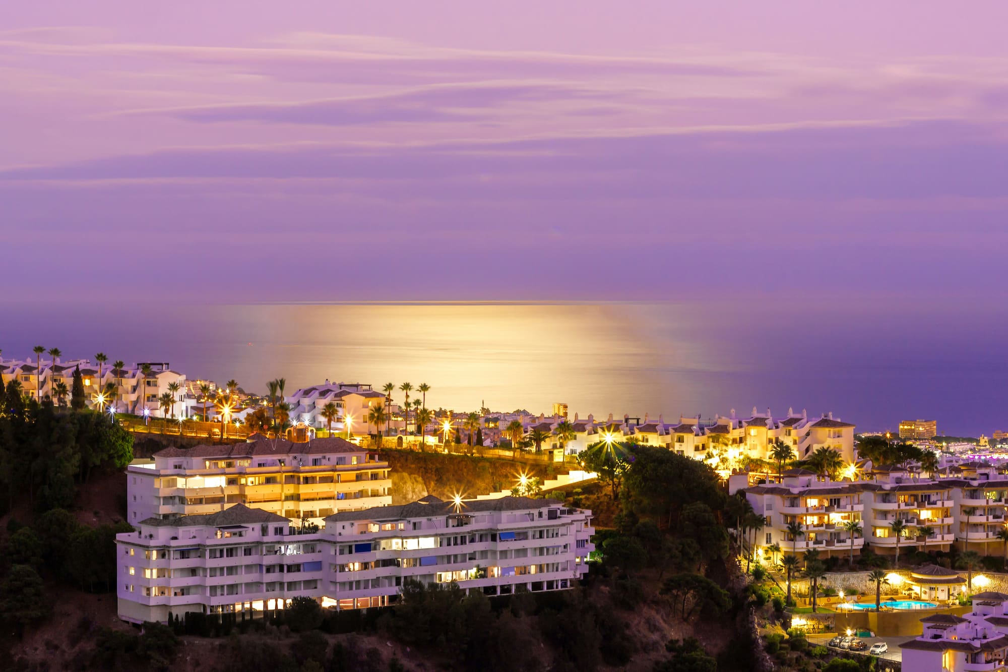 Illuminated coastal resort at twilight with palm trees and ocean view.